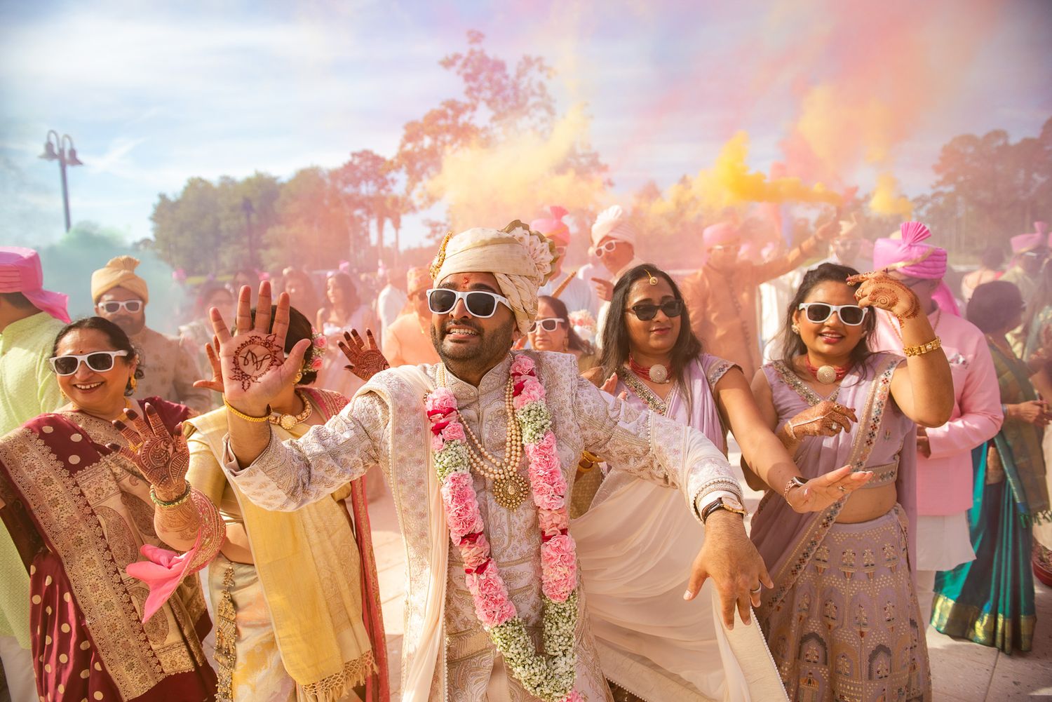 Colorful Holi celebration with wedding guests dancing amid pink powder clouds.