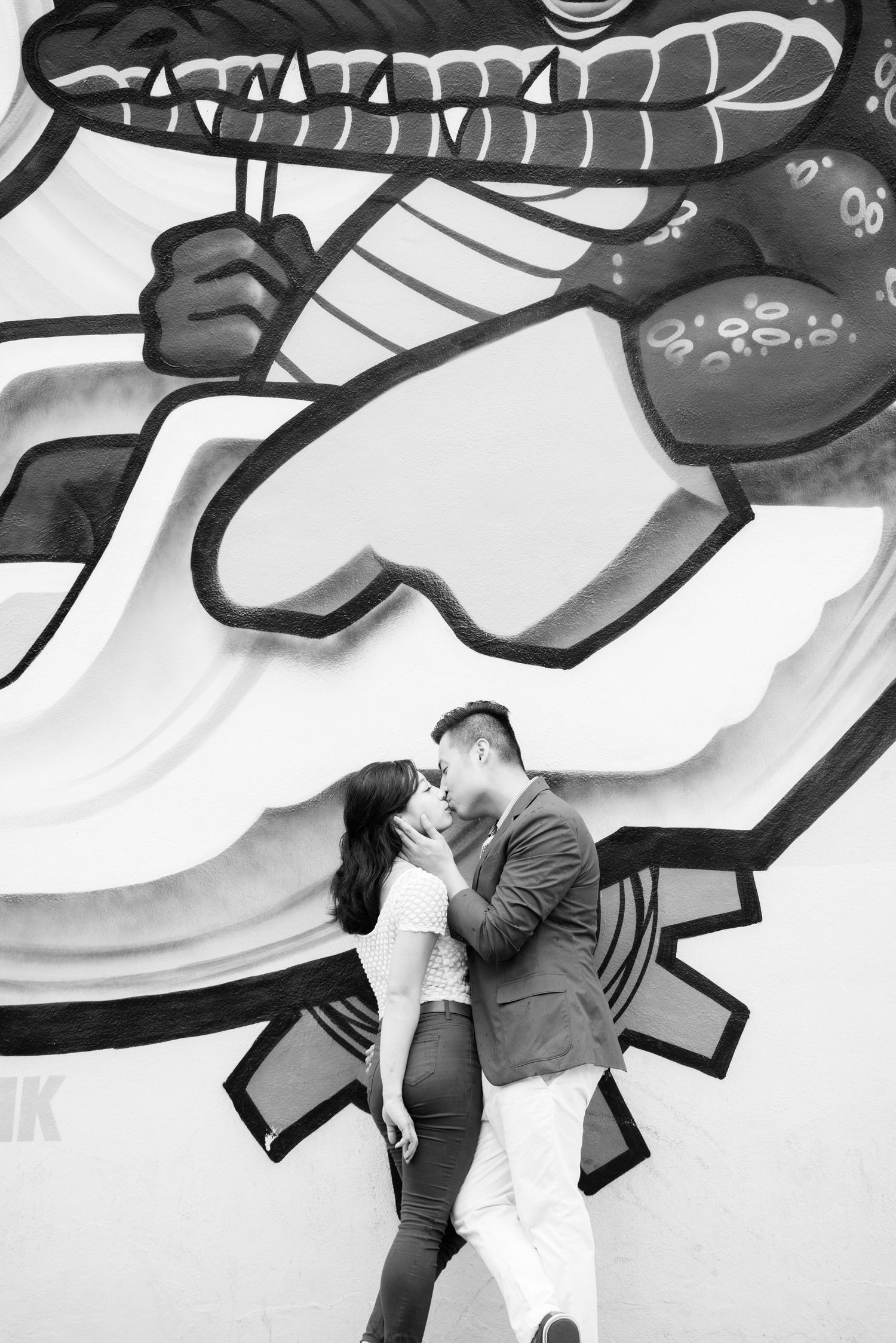 Couple kissing in front of black and white street art mural.