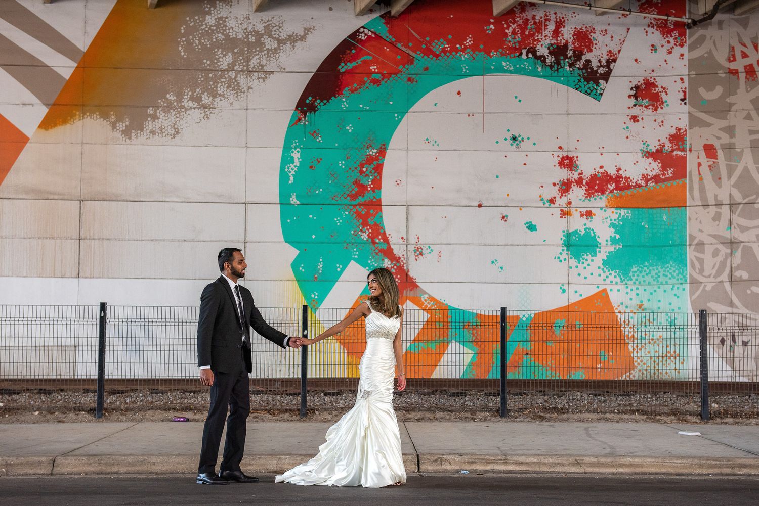 Wedding couple posing in front of colorful street art mural.