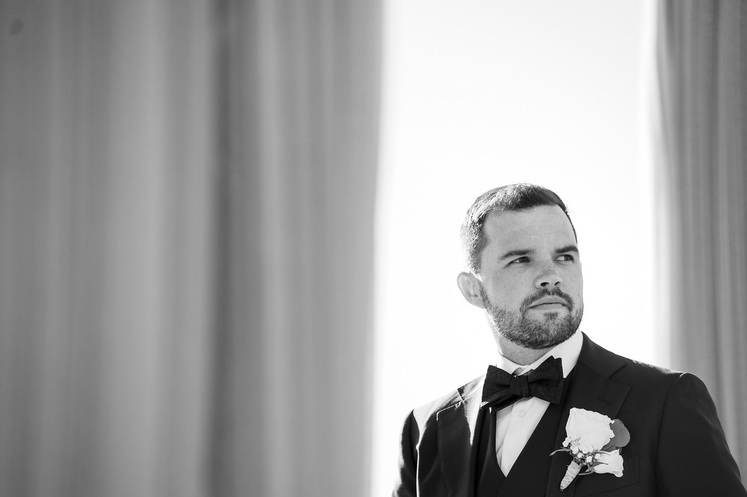 Black and white portrait with dramatic window lighting in formal wedding attire.