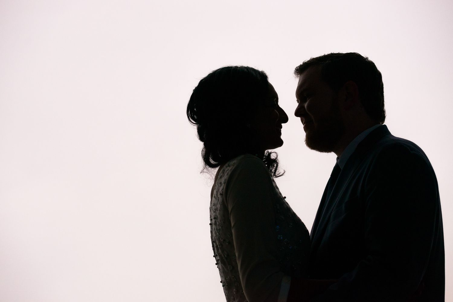 A silhouetted profile of a couple about to kiss against a light background.