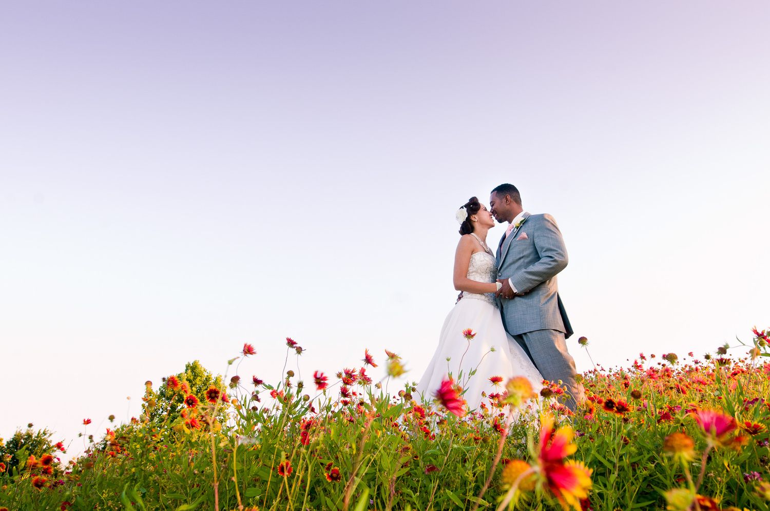 Couple shares romantic moment in wildflower field at sunset with red poppies in foreground.
