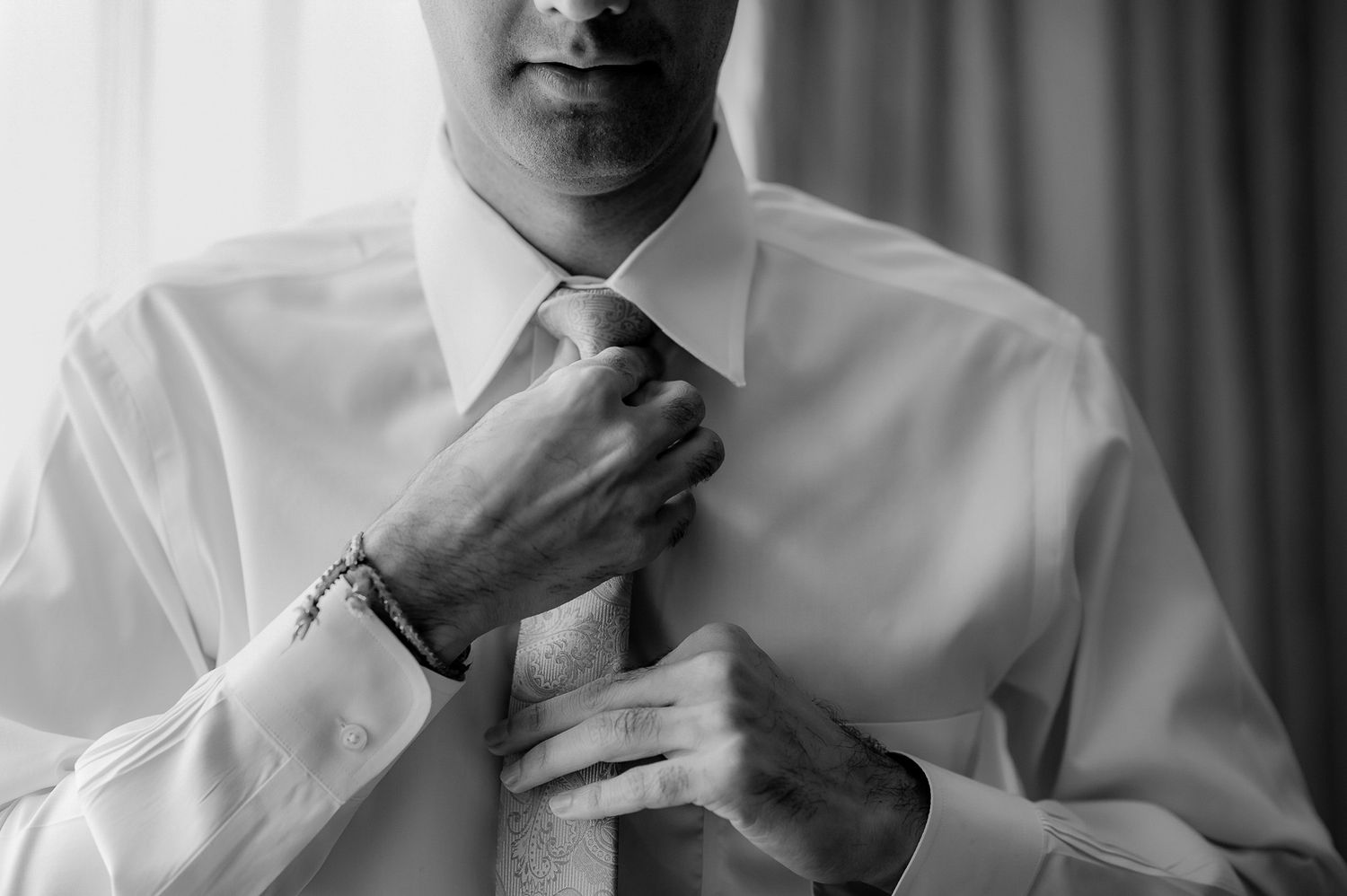 Close-up shot of someone adjusting a white tie while wearing a formal dress shirt.