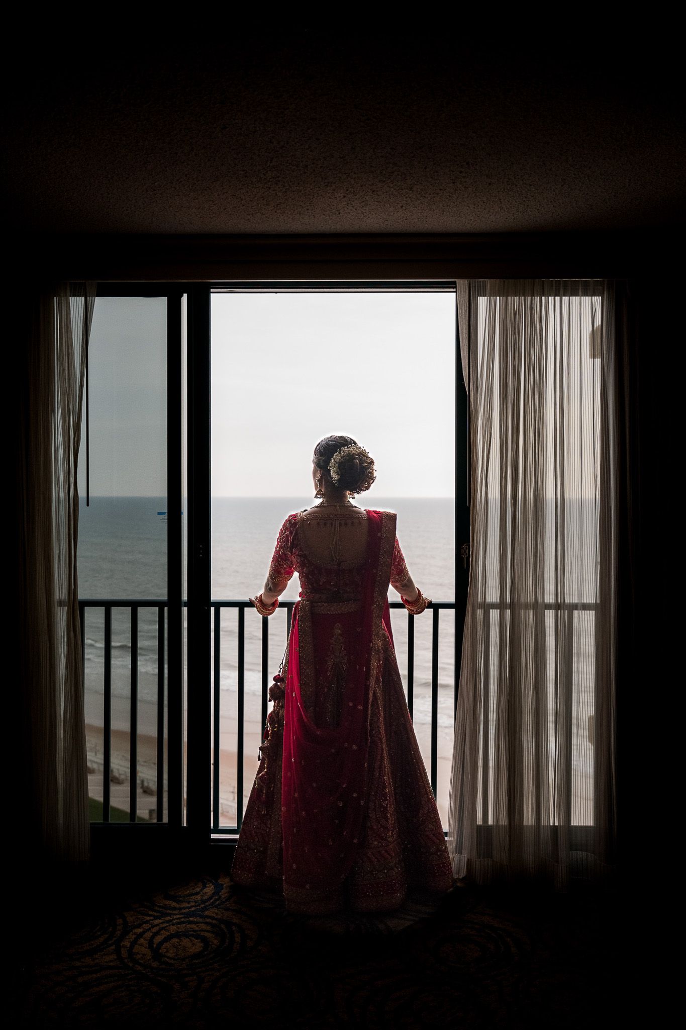 Silhouette through window frame of person in red dress looking at ocean view.