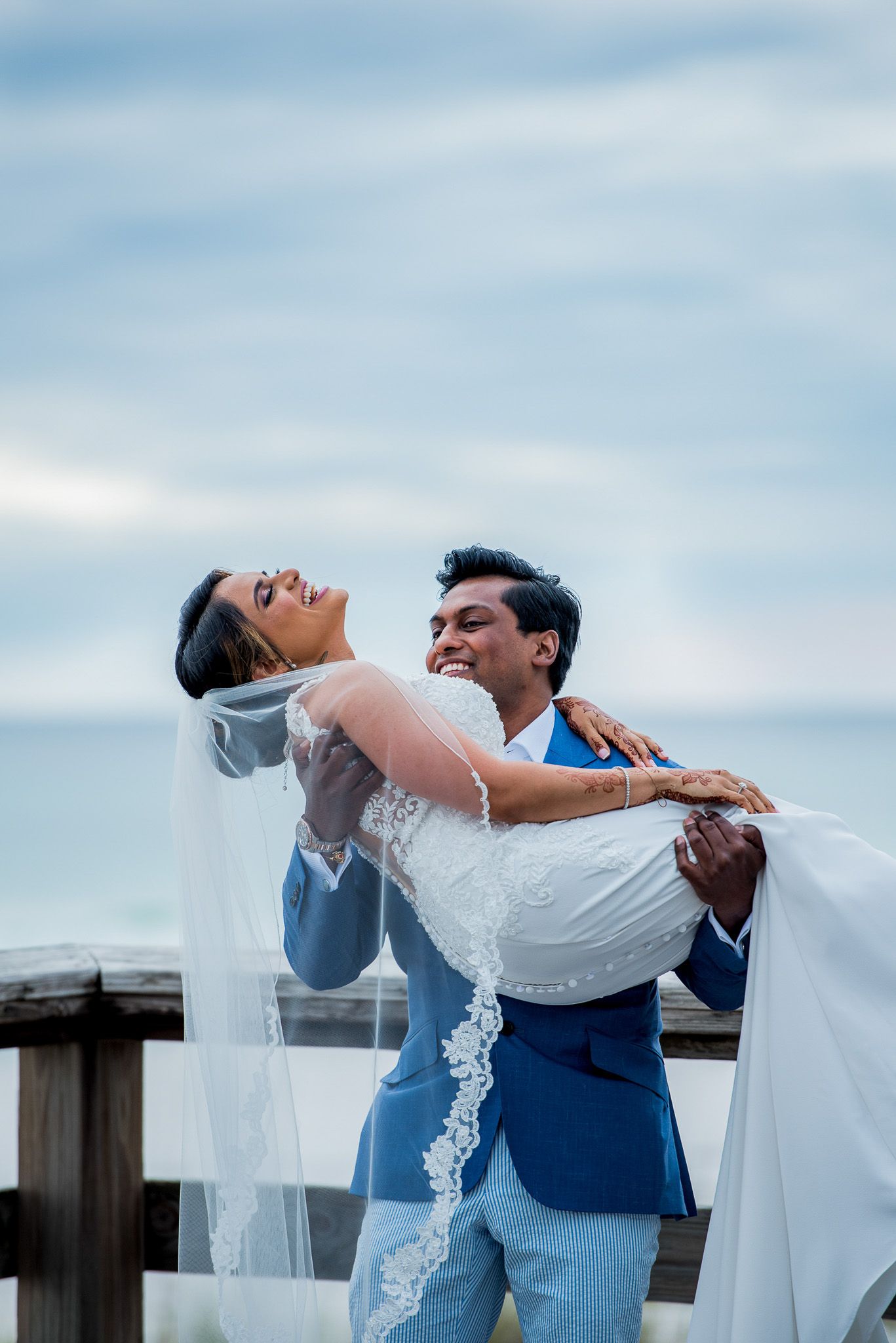 Joyful wedding moment captured on wooden boardwalk against blue sky.