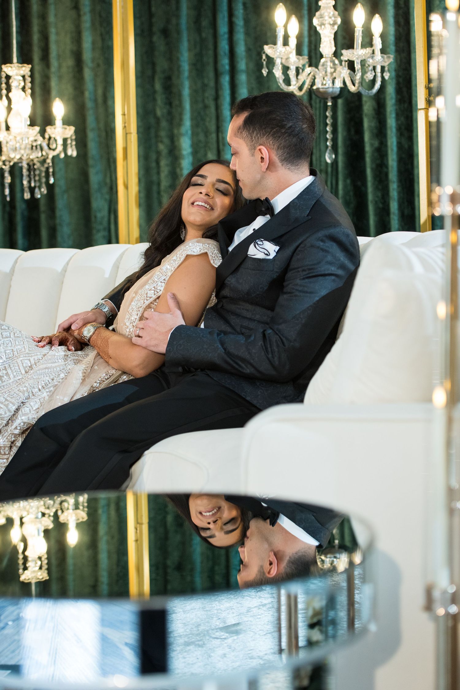 Romantic wedding couple relaxing on white sofa under crystal chandeliers.