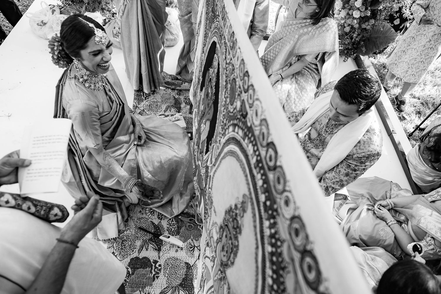 Black and white photo showing reflections in ornate mirror during wedding preparations.