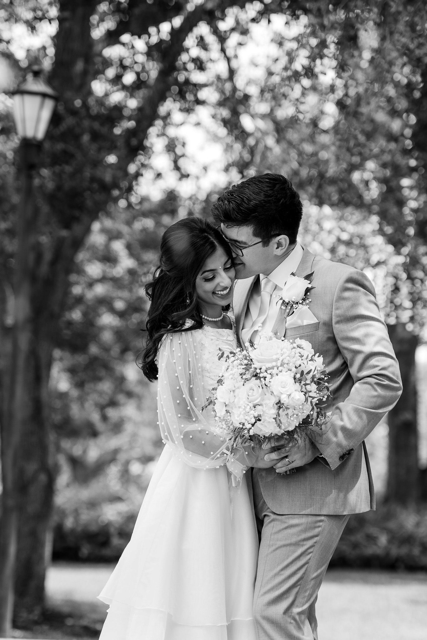 Romantic black and white wedding portrait of couple embracing in a garden.