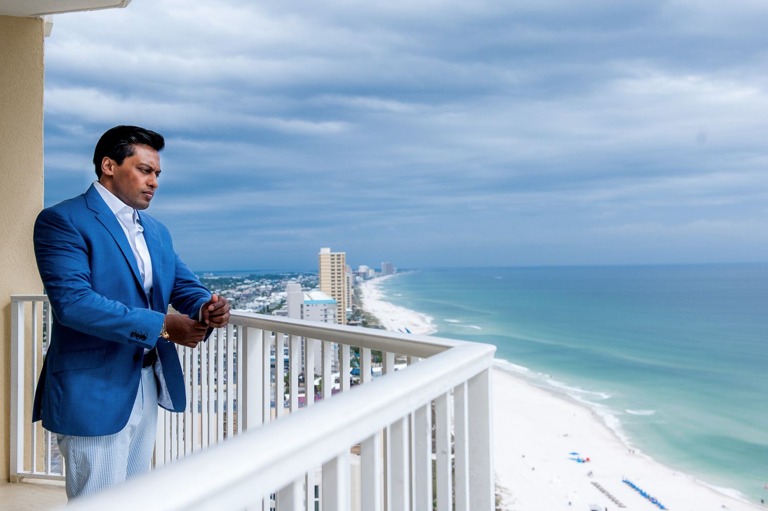 Person in blue blazer overlooking a stunning beachfront balcony view with turquoise waters.