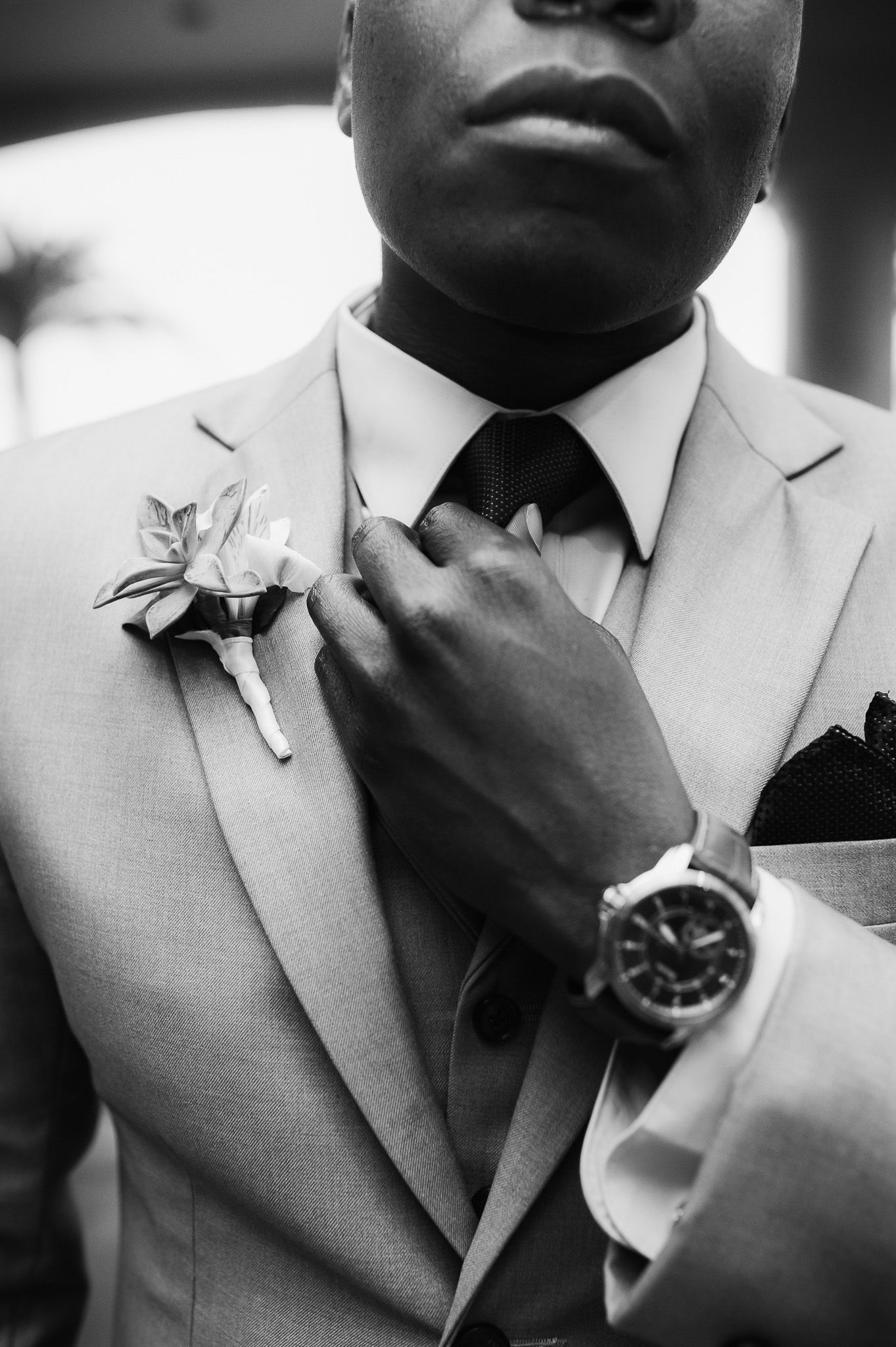 Close-up of groom in light gray suit adjusting boutonniere and wearing elegant watch.