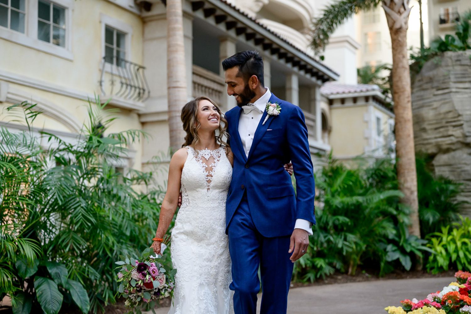 Happy couple in wedding attire posing together in front of luxury venue with garden.