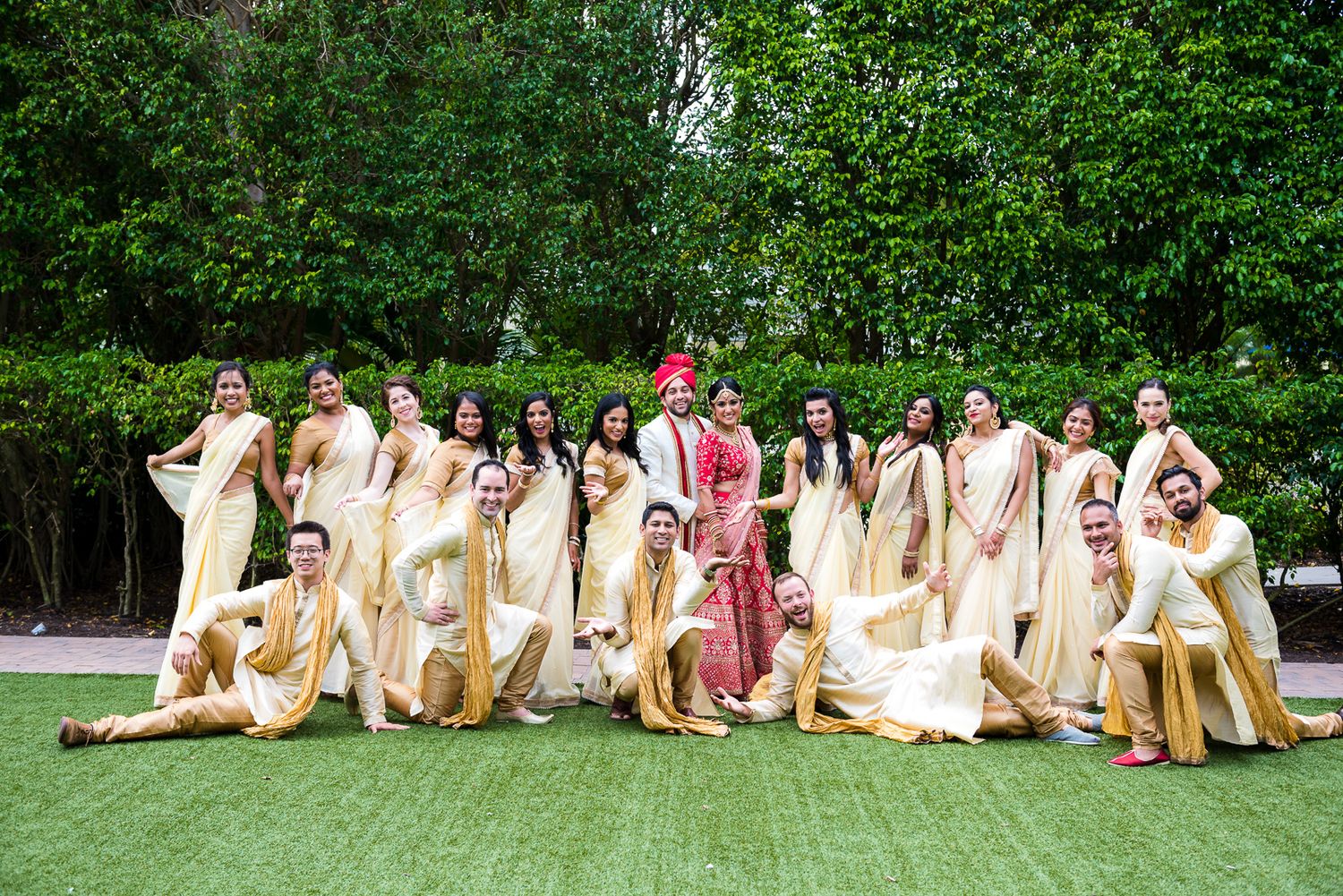 Wedding party in cream and maroon traditional Indian attire posing on green lawn.