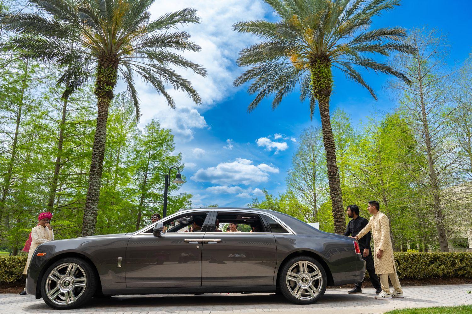 Luxury silver car parked between palm trees under bright blue sky.
