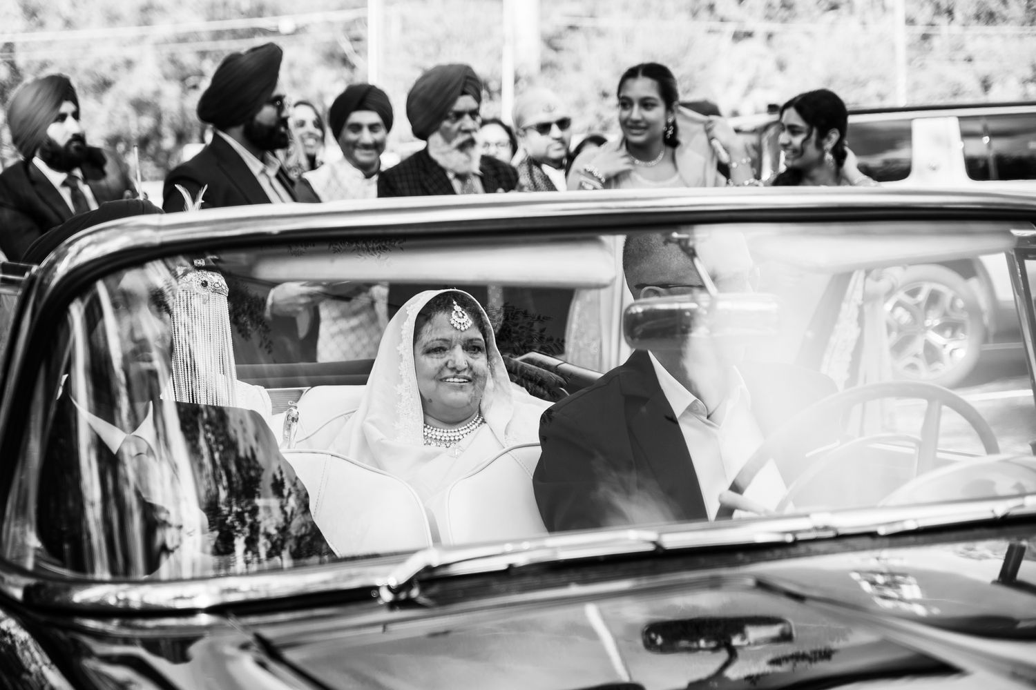 Vintage black and white photo of newlyweds waving from classic car window.