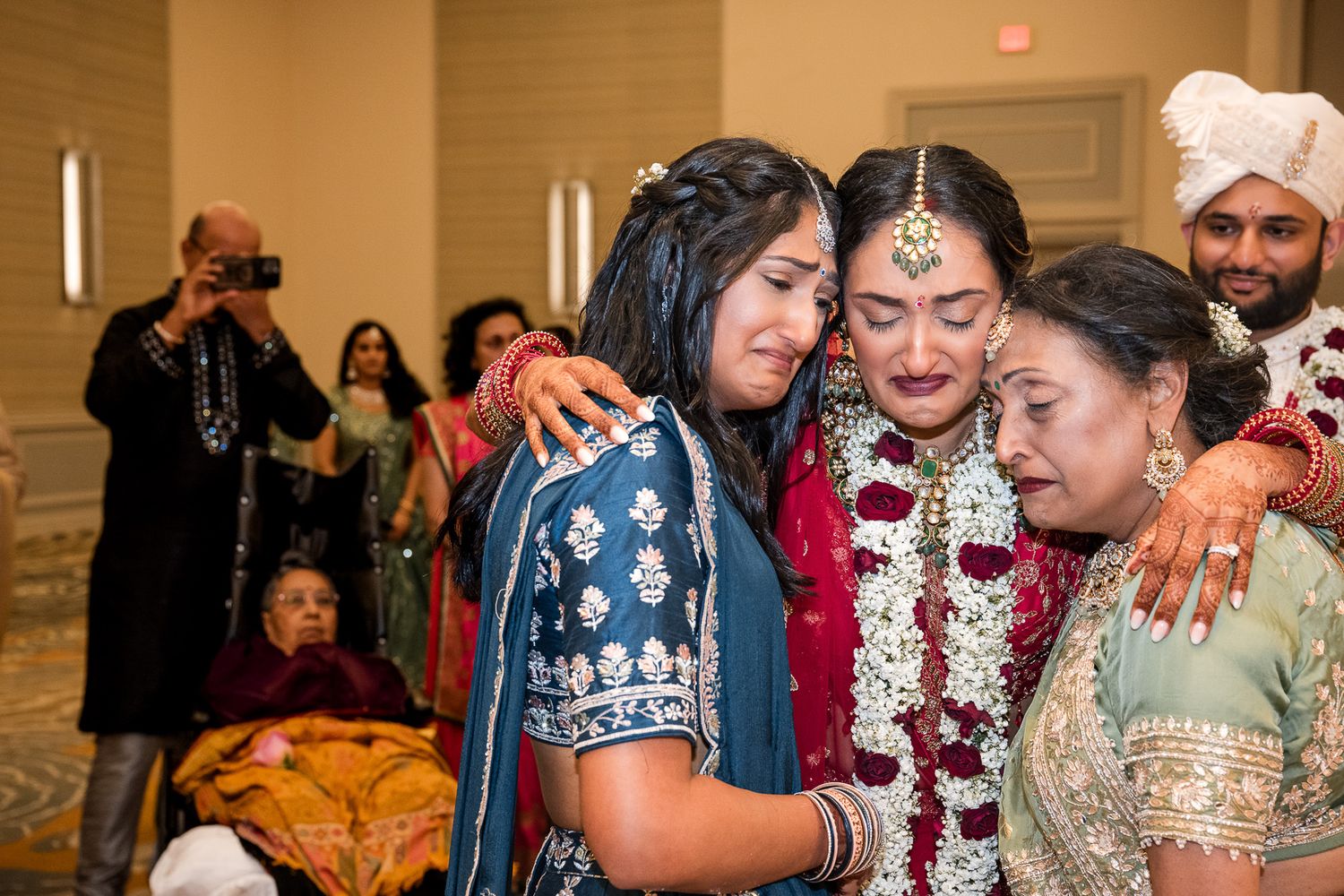 Group sharing emotional embraces during an Indian wedding ceremony in traditional attire.