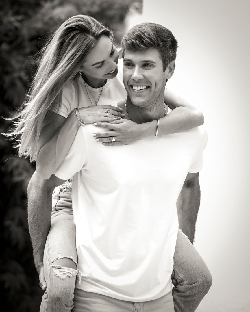 Couple sharing playful piggyback ride moment outdoors in black and white photo.