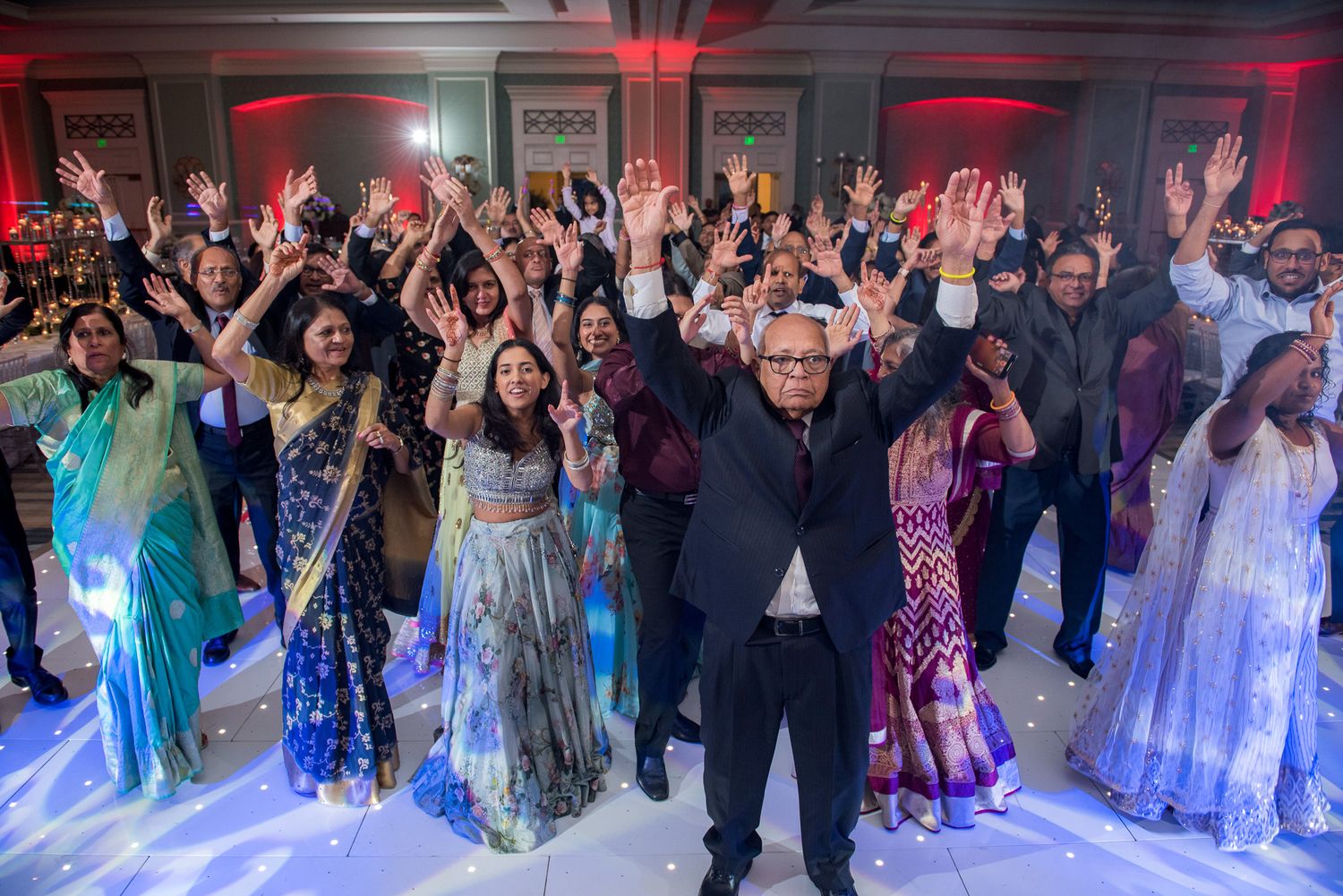 Wedding reception dance party with crowd celebrating under red mood lighting.