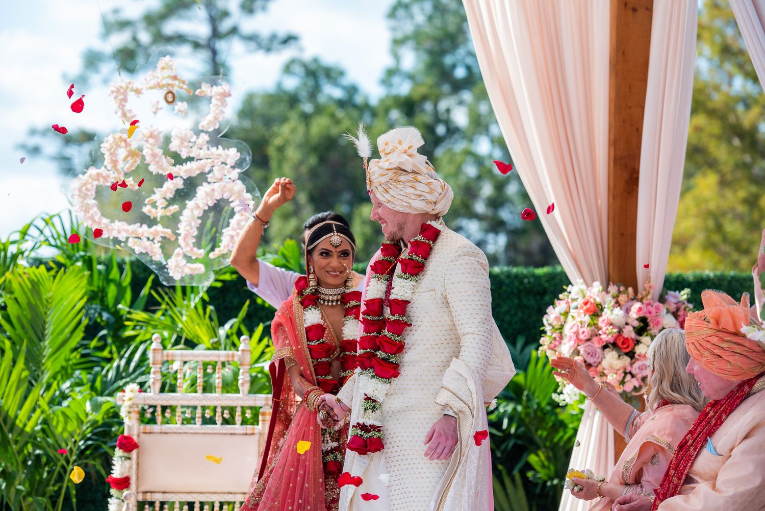 Wedding ceremony under floral mandap with bride and groom exchanging garlands.