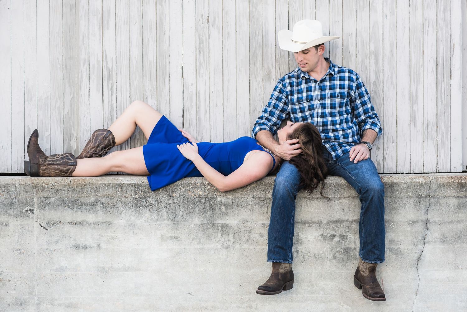 Casual engagement photo with couple in rustic setting against white wooden wall.