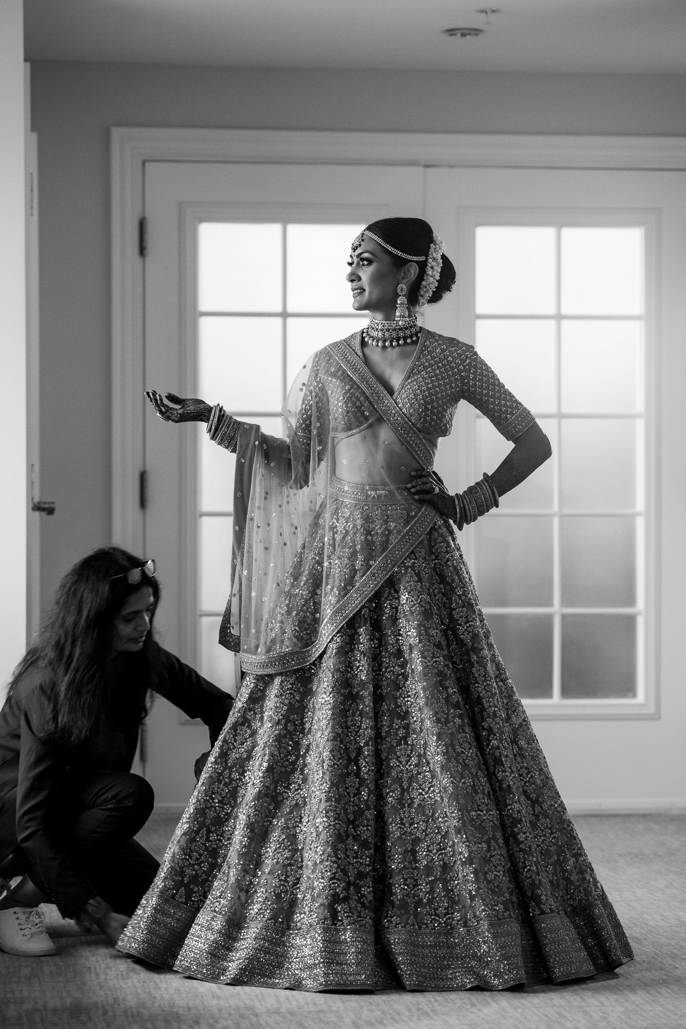 Traditional Indian bride in embellished lehenga getting final adjustments from stylist.