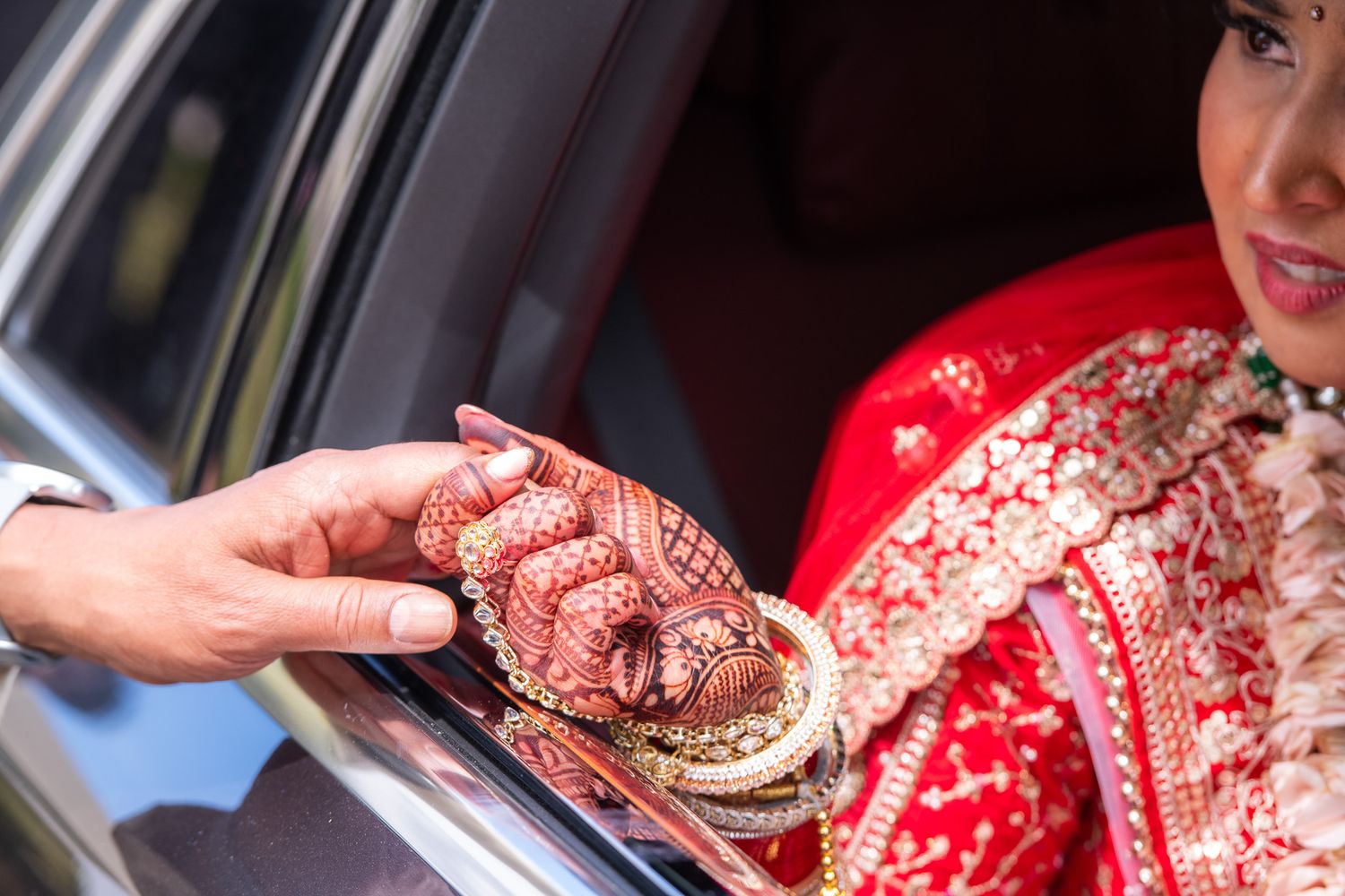 Close-up of ornate henna-decorated hands exchanging jewelry through car window.