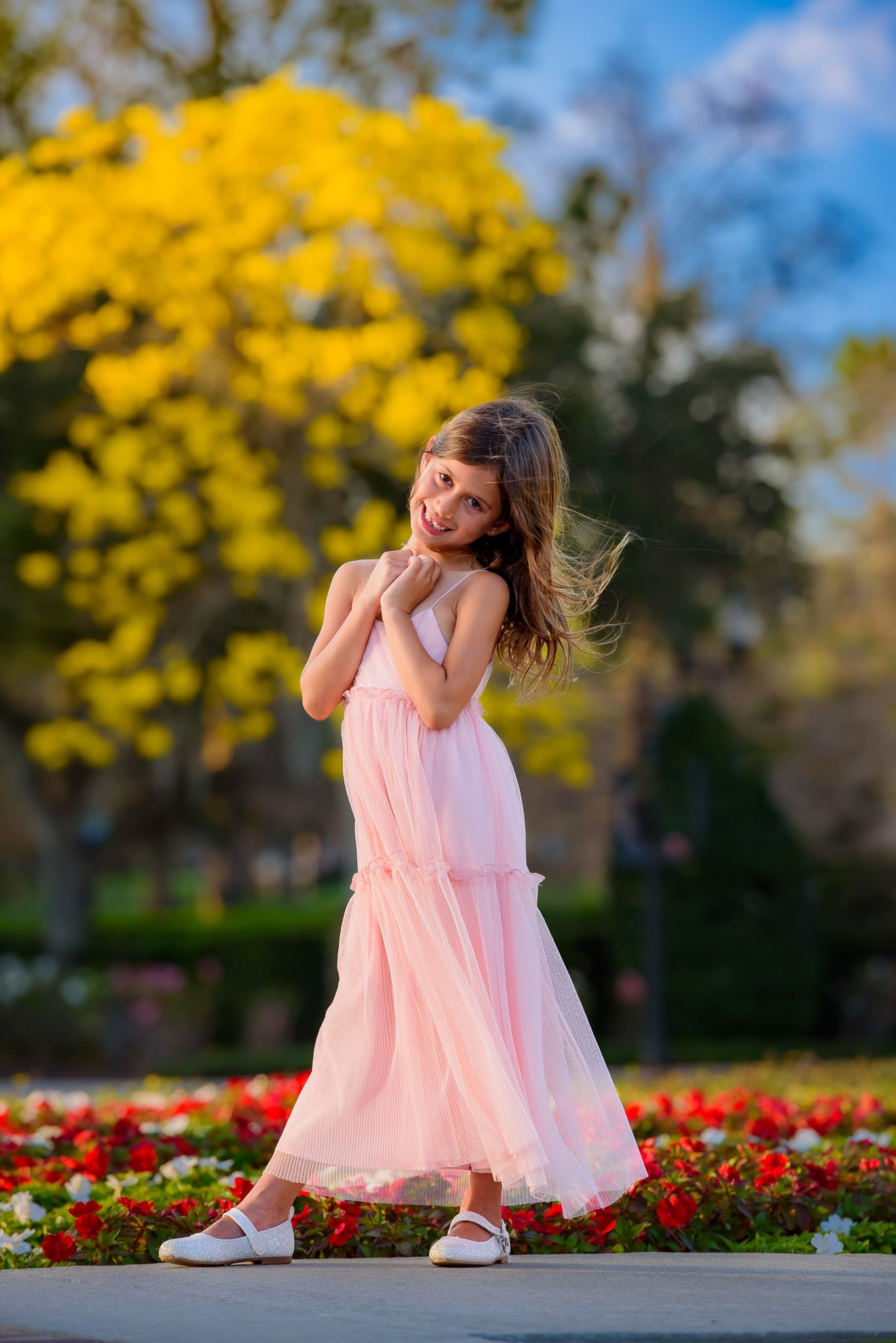 Young dancer in pink dress twirling in a garden with yellow trees and red flowers.