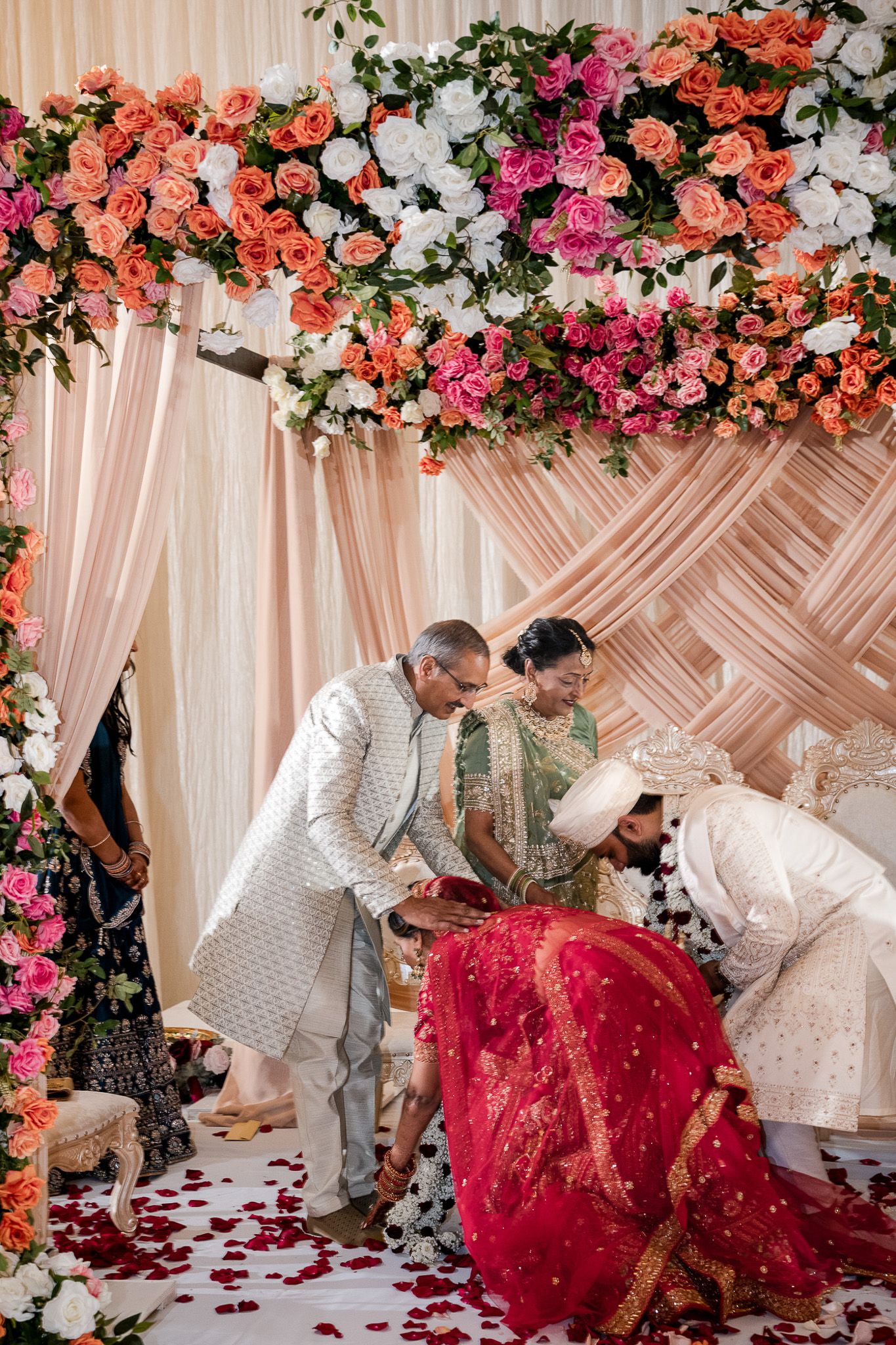 Wedding ceremony under floral arch with pink and coral roses during traditional Indian rituals.