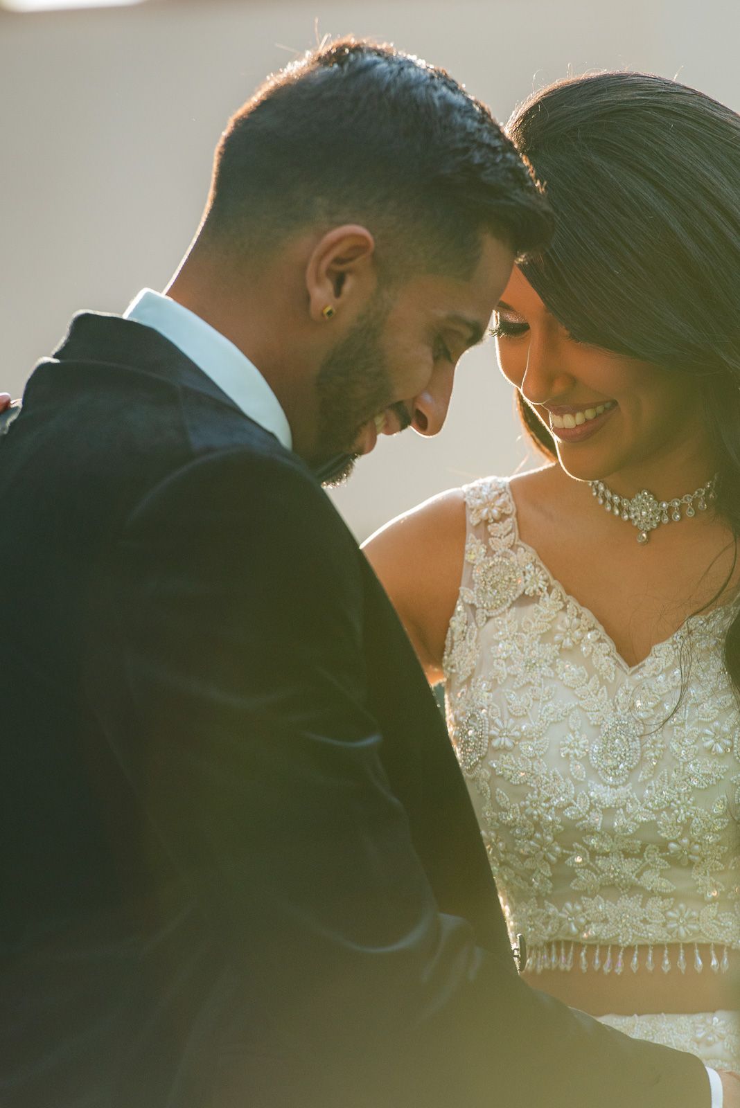 Intimate sunlit moment between couple in formal wedding attire.