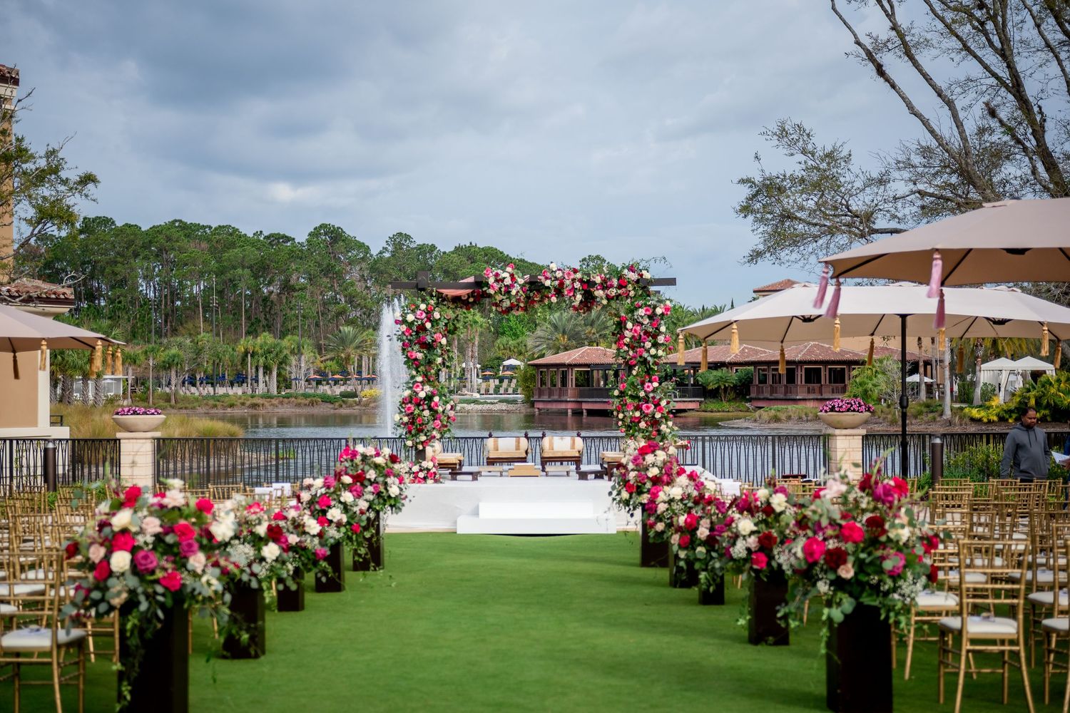 Outdoor wedding ceremony setup with pink floral arch and lakeside view.