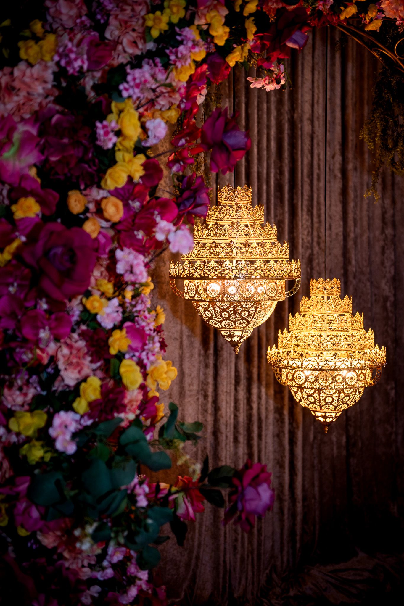 Ornate golden lanterns hanging amidst colorful floral decorations at a wedding venue.