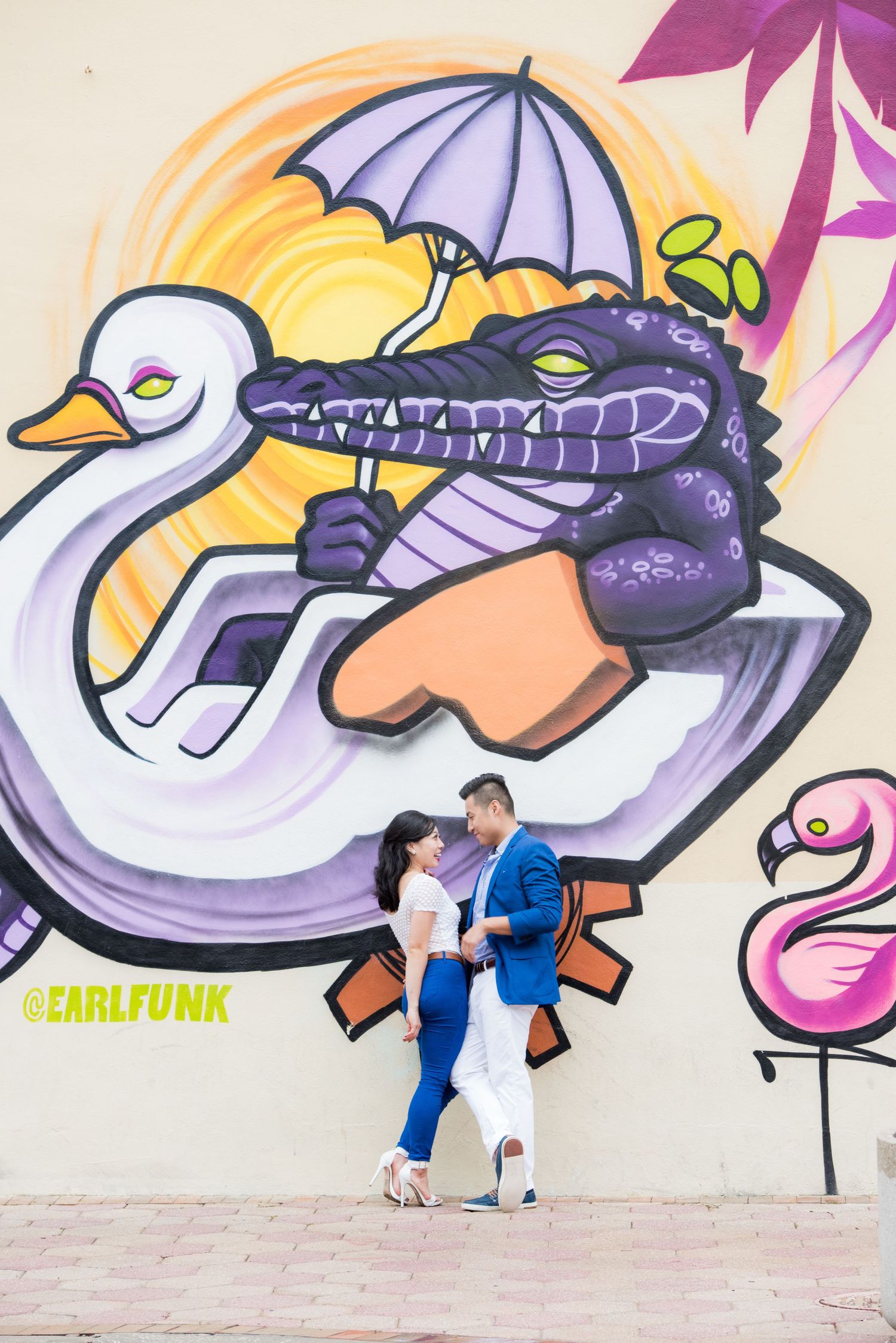 Couple posing in front of colorful street art featuring a duck and alligator design.