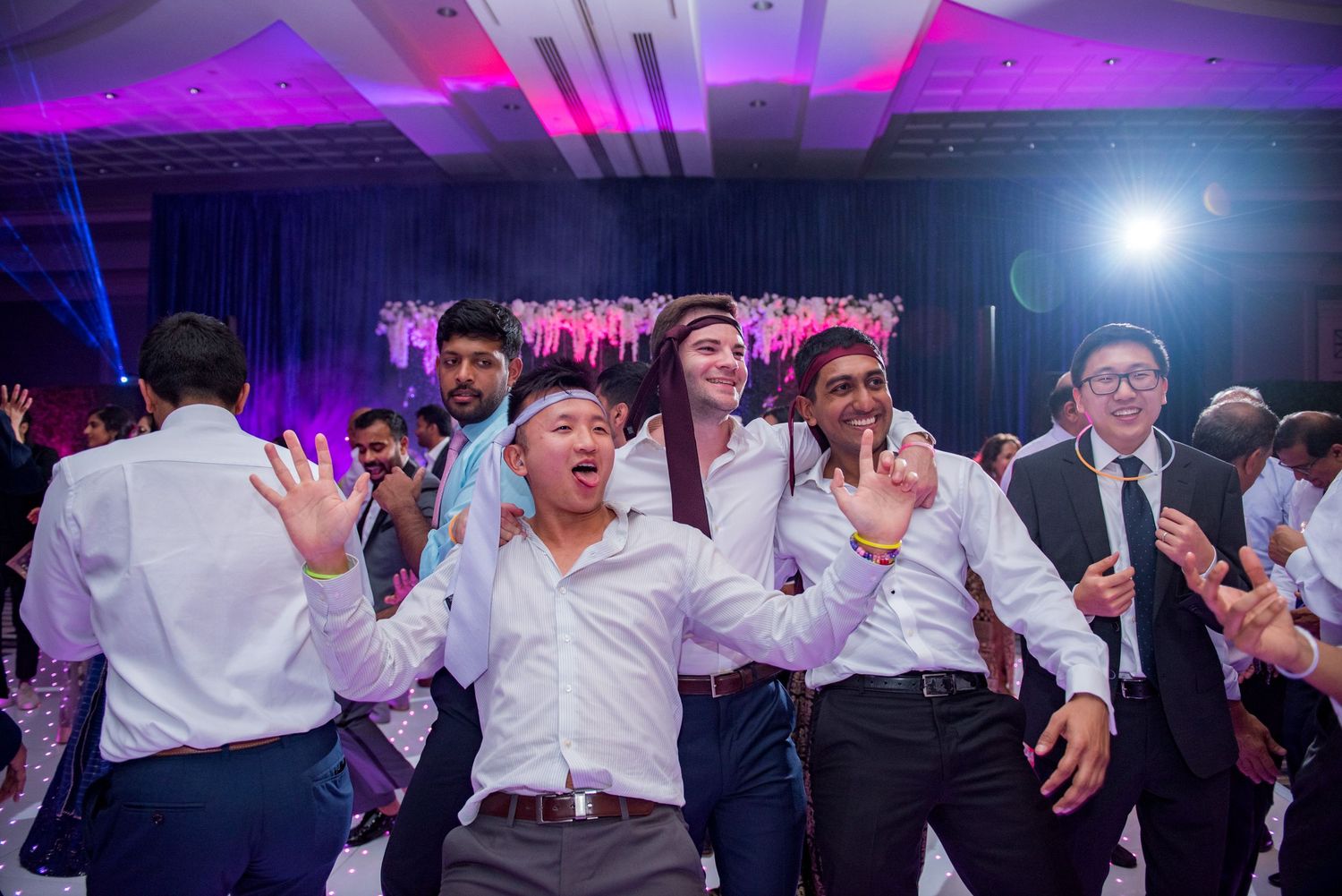 Wedding guests dancing under purple lighting at a modern reception venue.