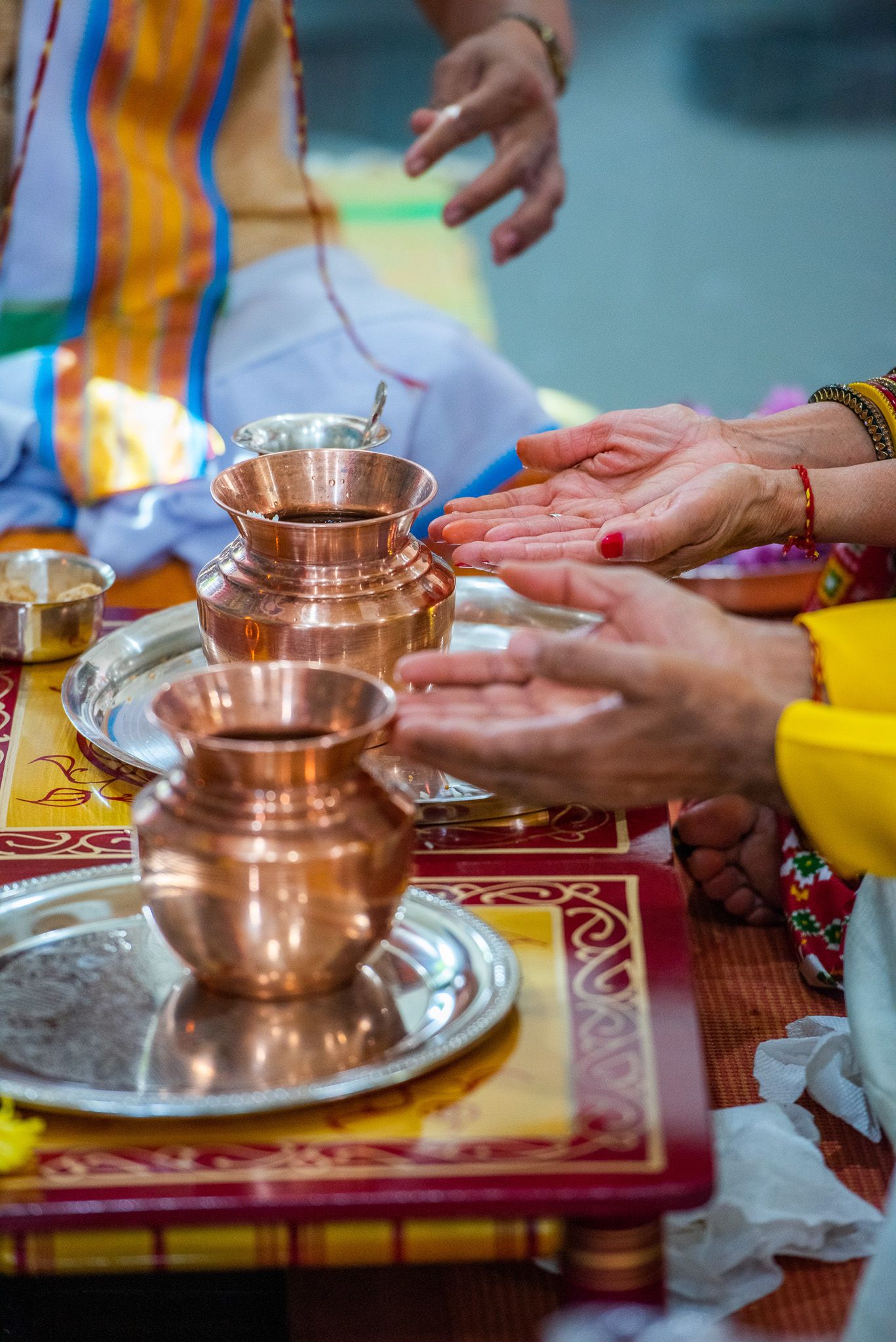 Traditional Hindu ceremony showing hands over copper vessels during sacred ritual.