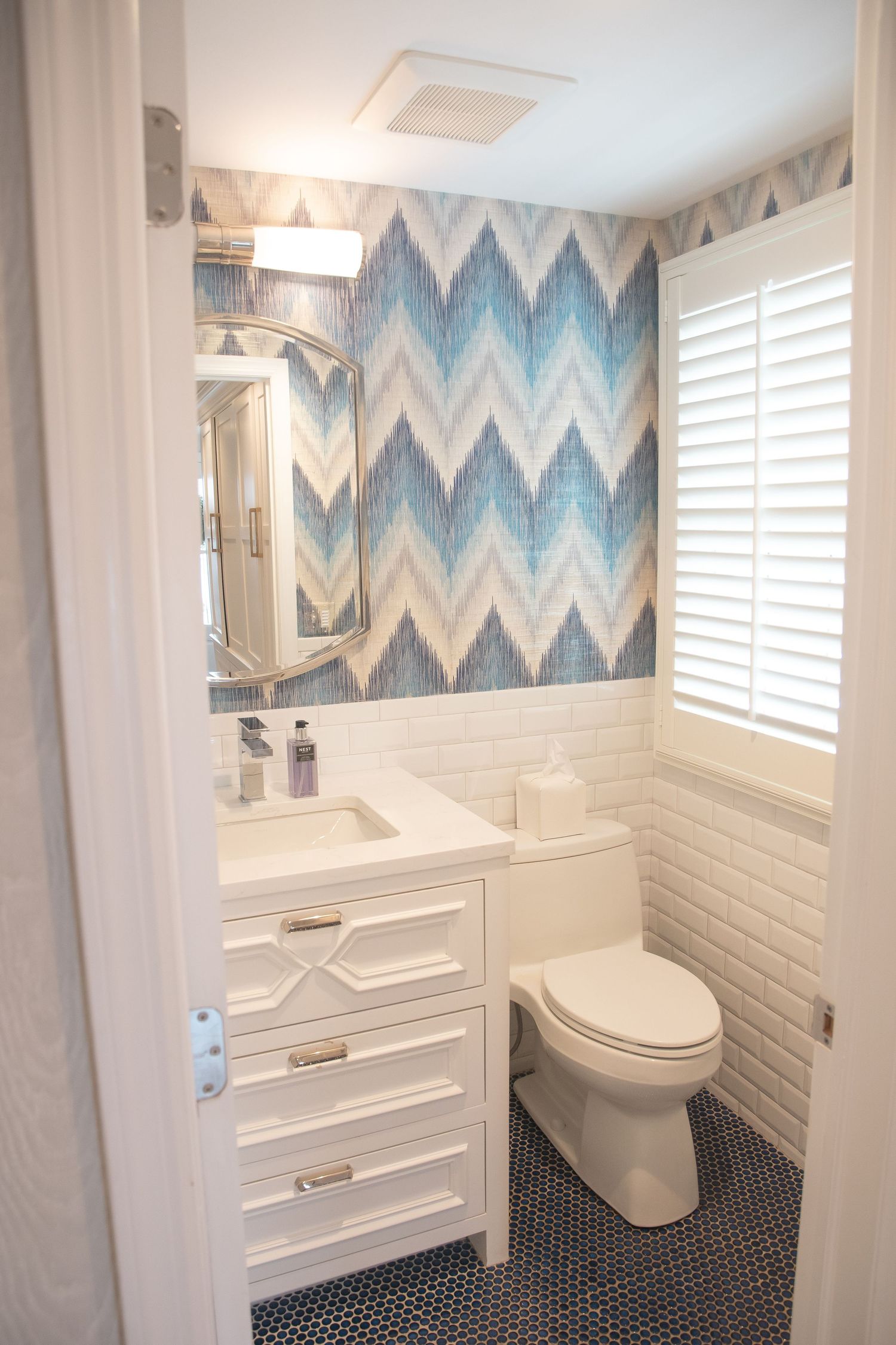 Modern bathroom interior with blue chevron wallpaper, white subway tile, and black floor tiles.