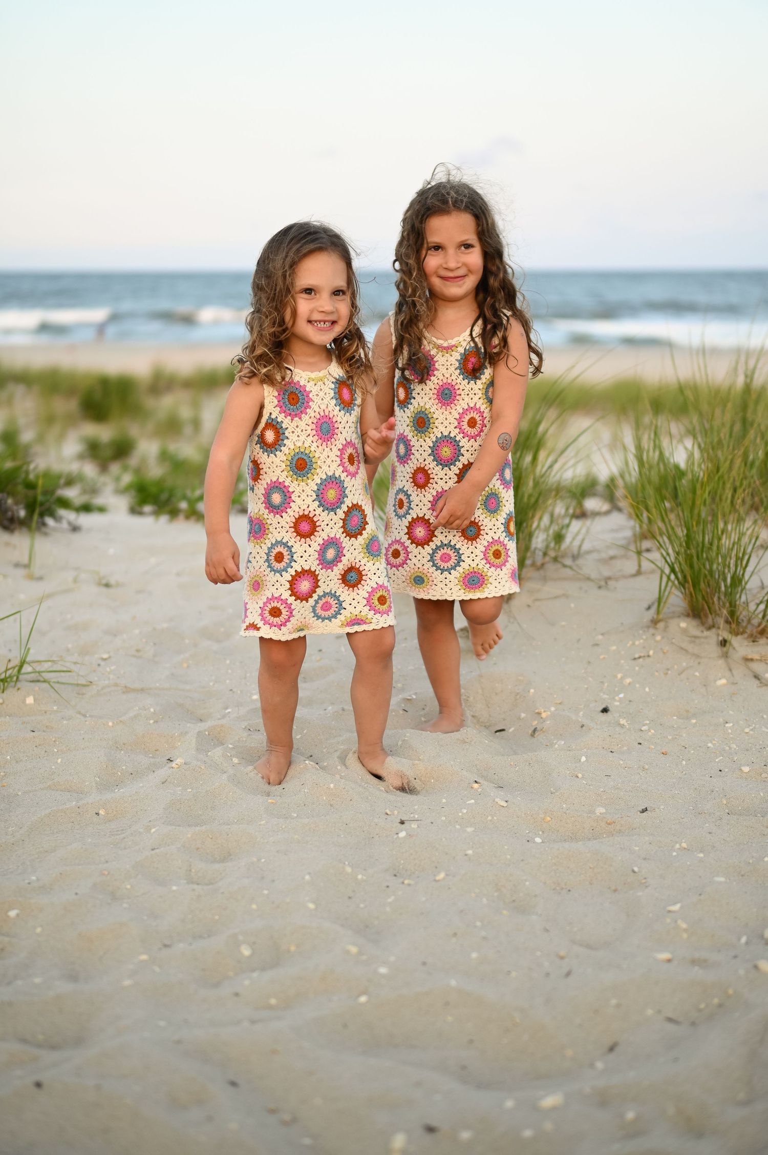Two young children in matching floral dresses playing on the beach at sunset.
