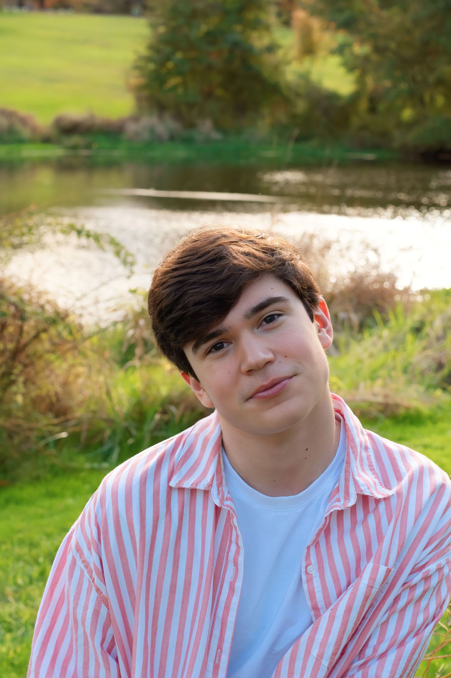 Portrait series in a grassy field wearing a pink striped button-down shirt and white t-shirt.