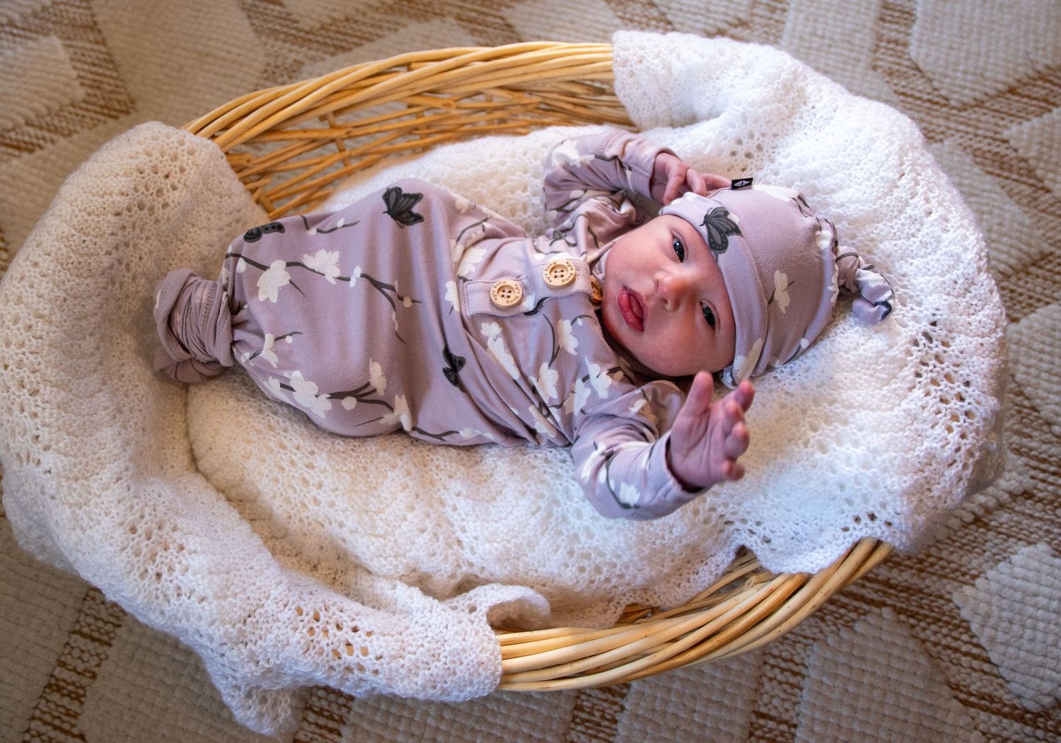 Newborn resting peacefully in white knit blanket inside woven basket.