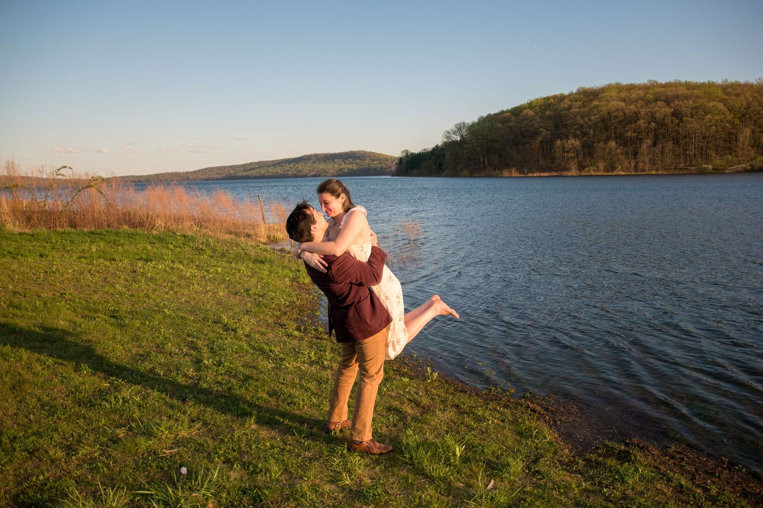 Playful interaction between couple on grassy hill overlooking lake.