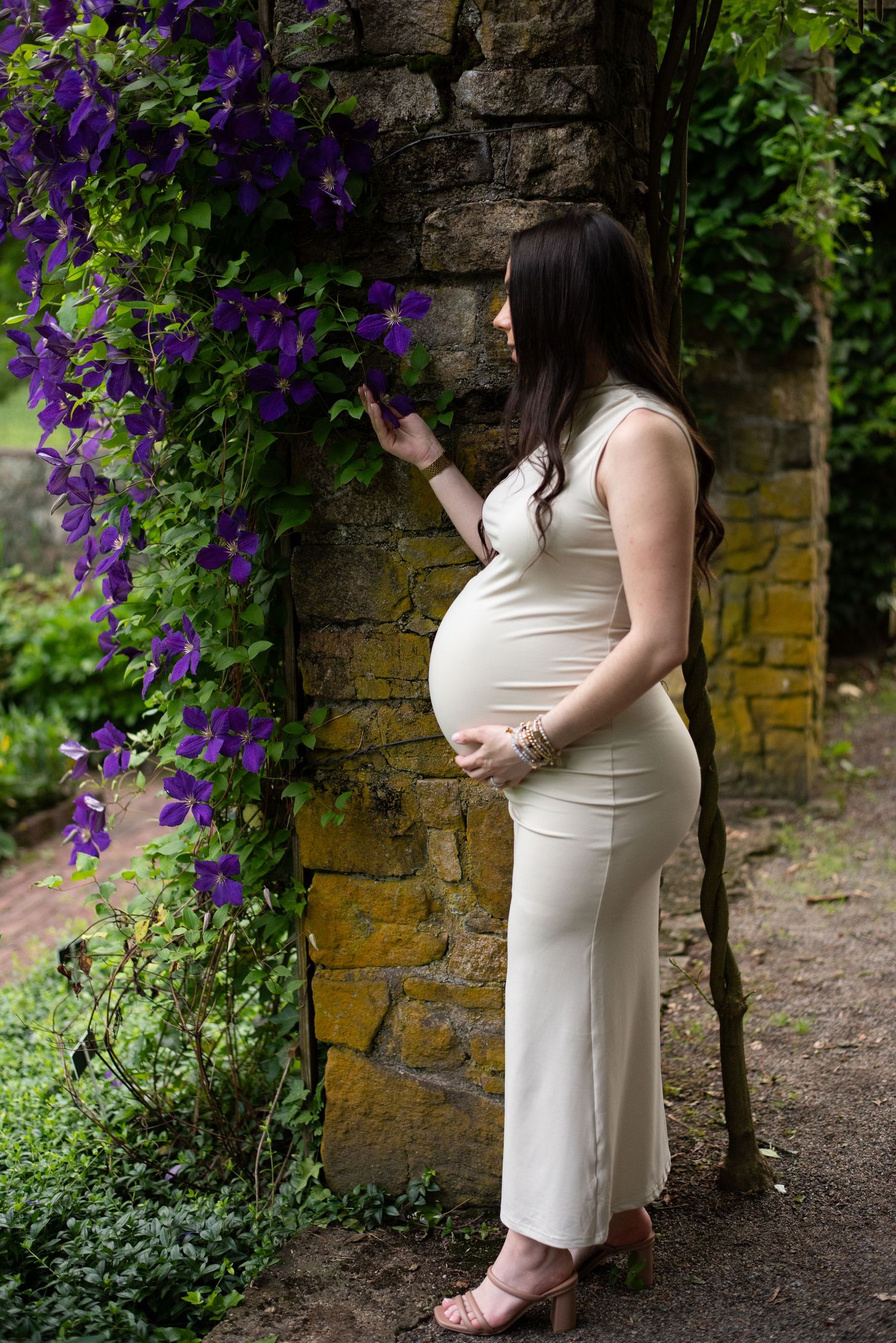 Elegant maternity portraits against a stone wall with cascading purple flowers.