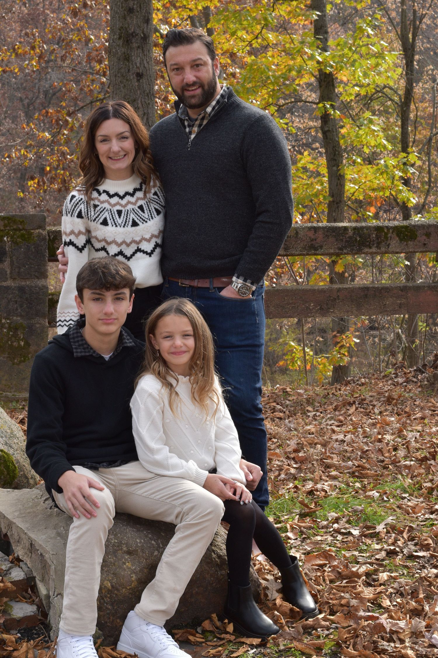 Family portrait session in autumn with fallen leaves and stone wall backdrop.
