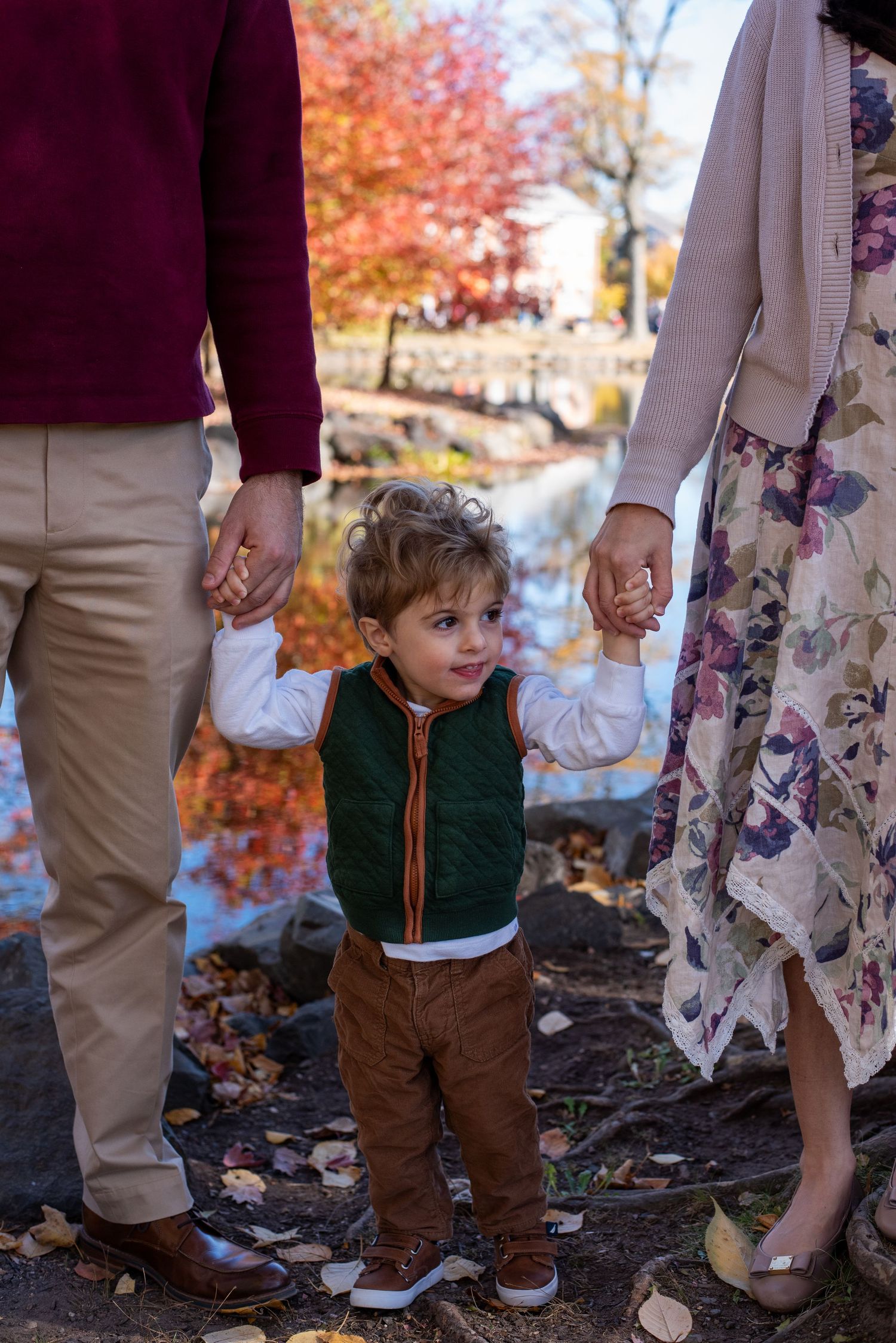 Small child holding hands with adults among fall foliage.