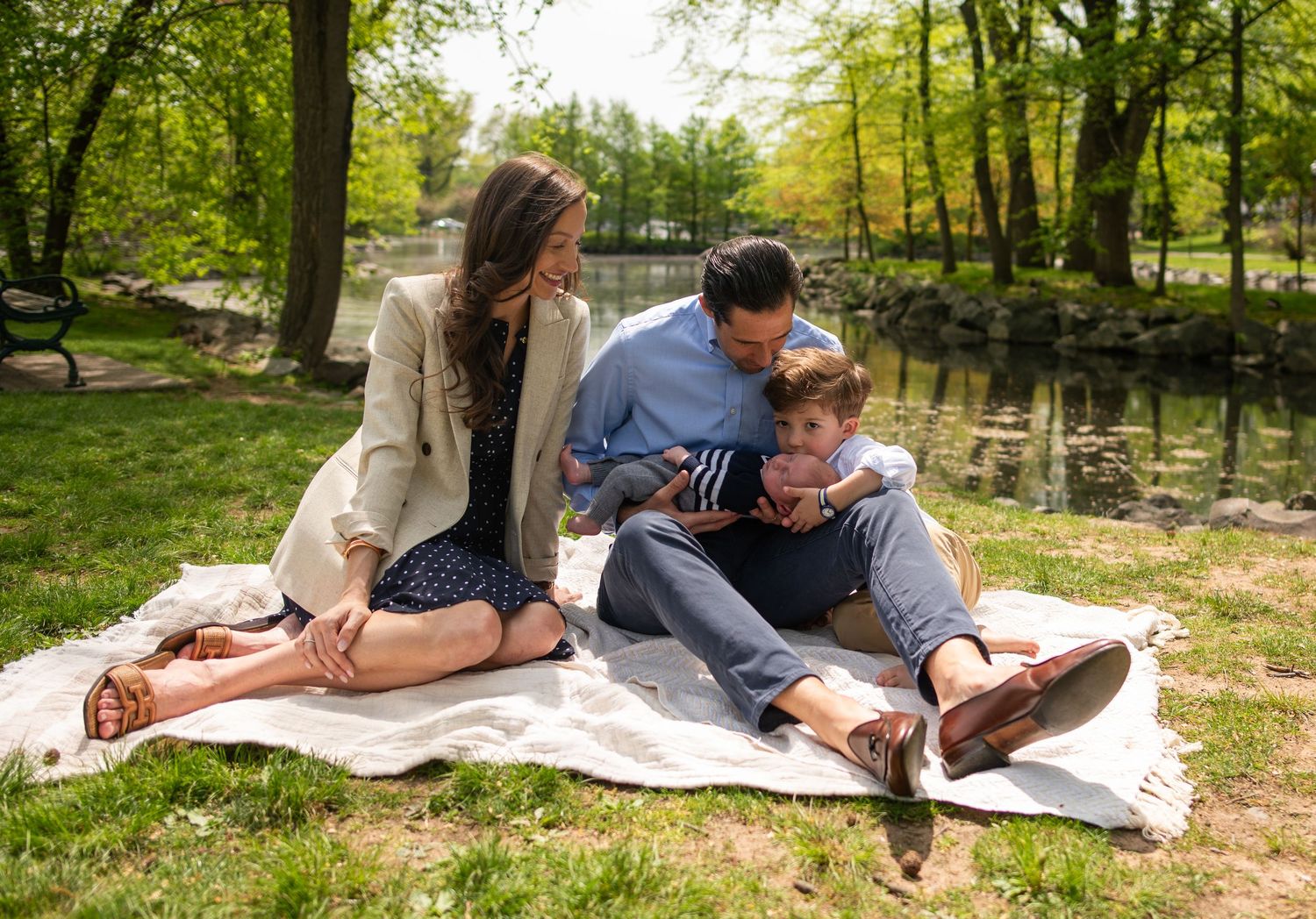 People relaxing on a blanket beneath green trees in a peaceful park setting.