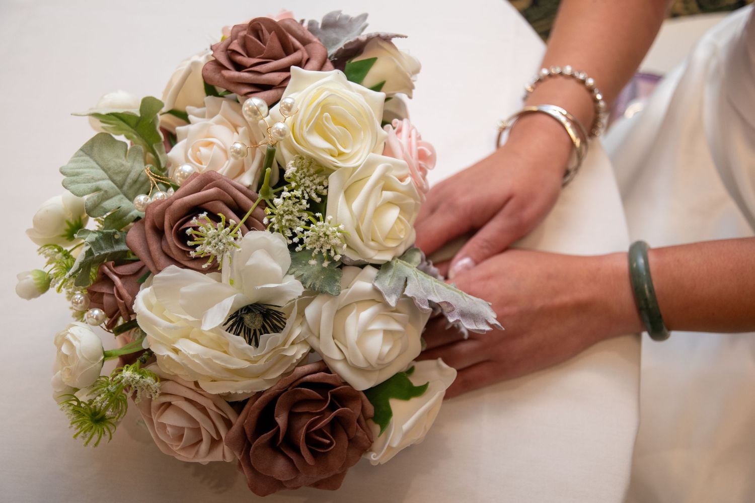 Close-up of hands arranging cream and mauve roses in a wedding bouquet.