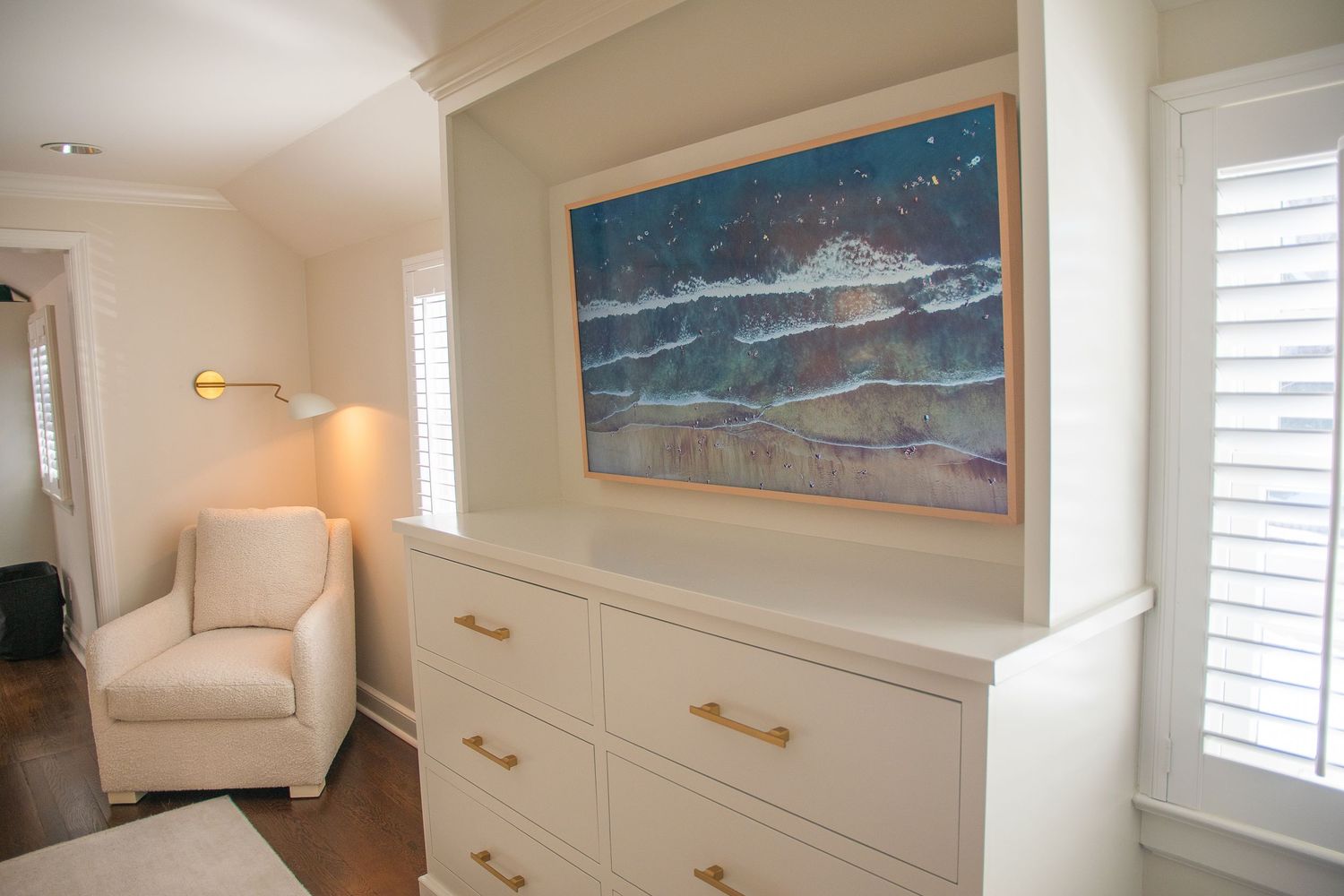 Light-filled room with built-in shelving, coastal artwork, and comfortable seating area.