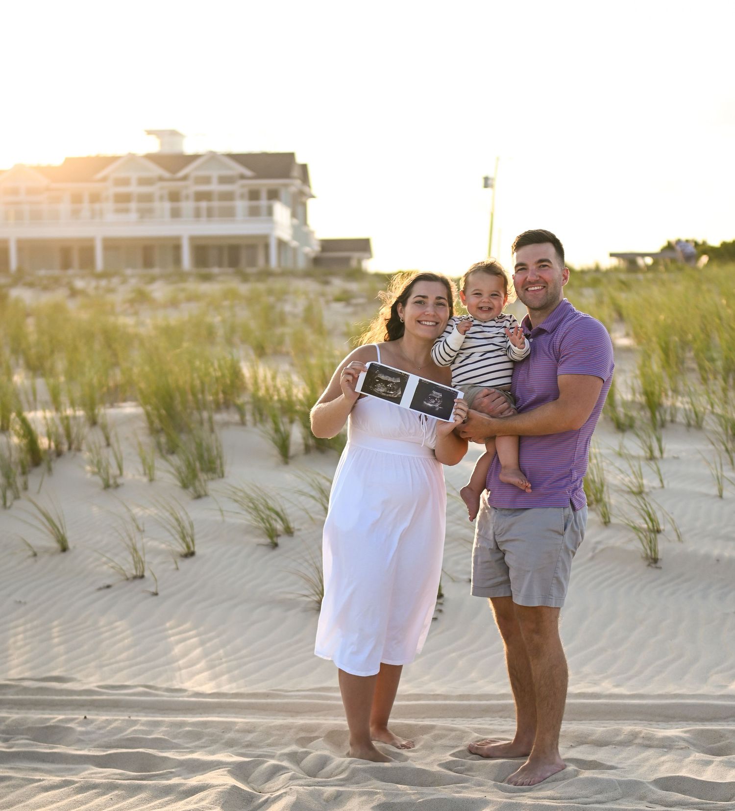 Family enjoying sunset on a sandy beach with dune grass in the background.