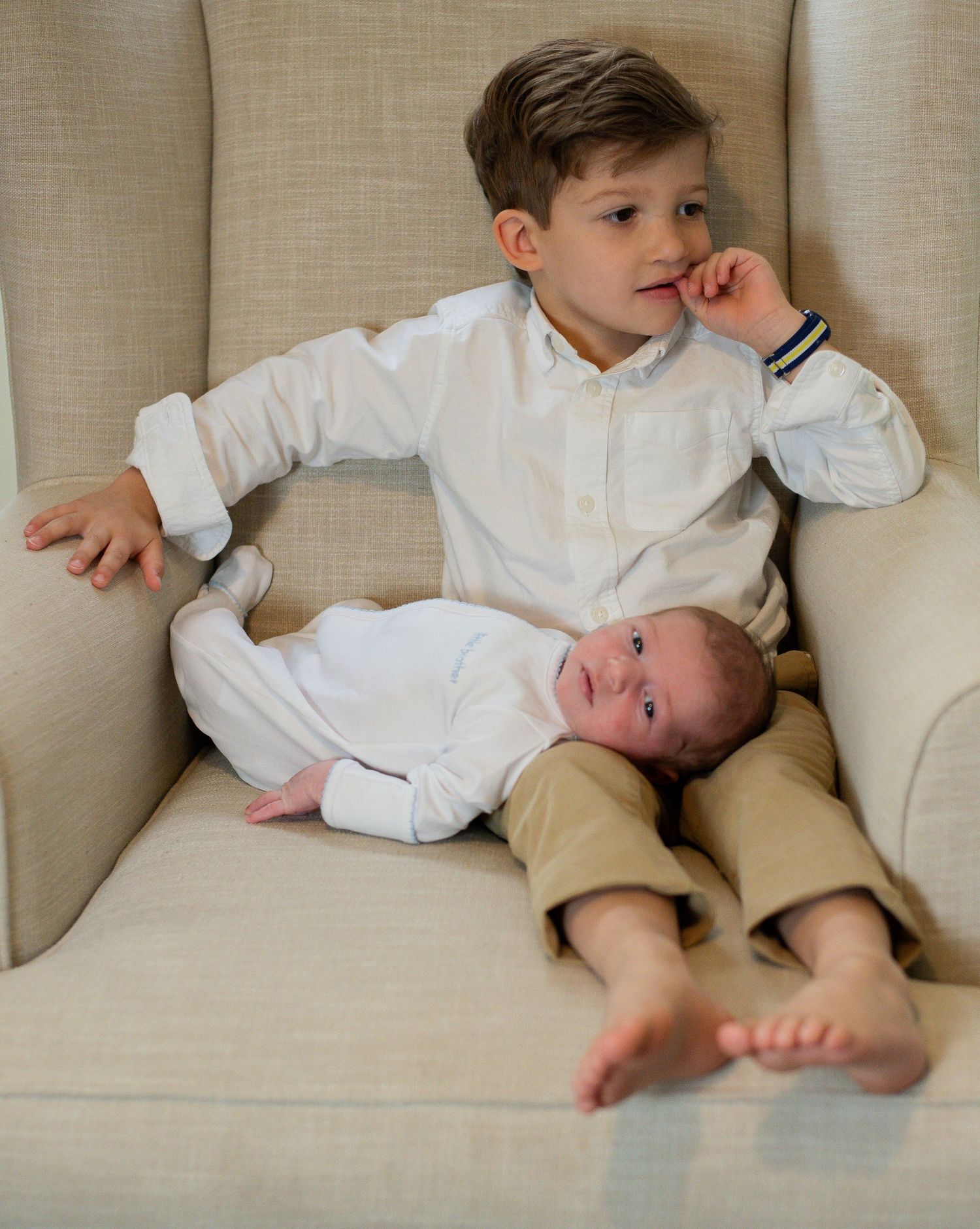 Two children lounging on a beige couch share a sweet sibling moment.