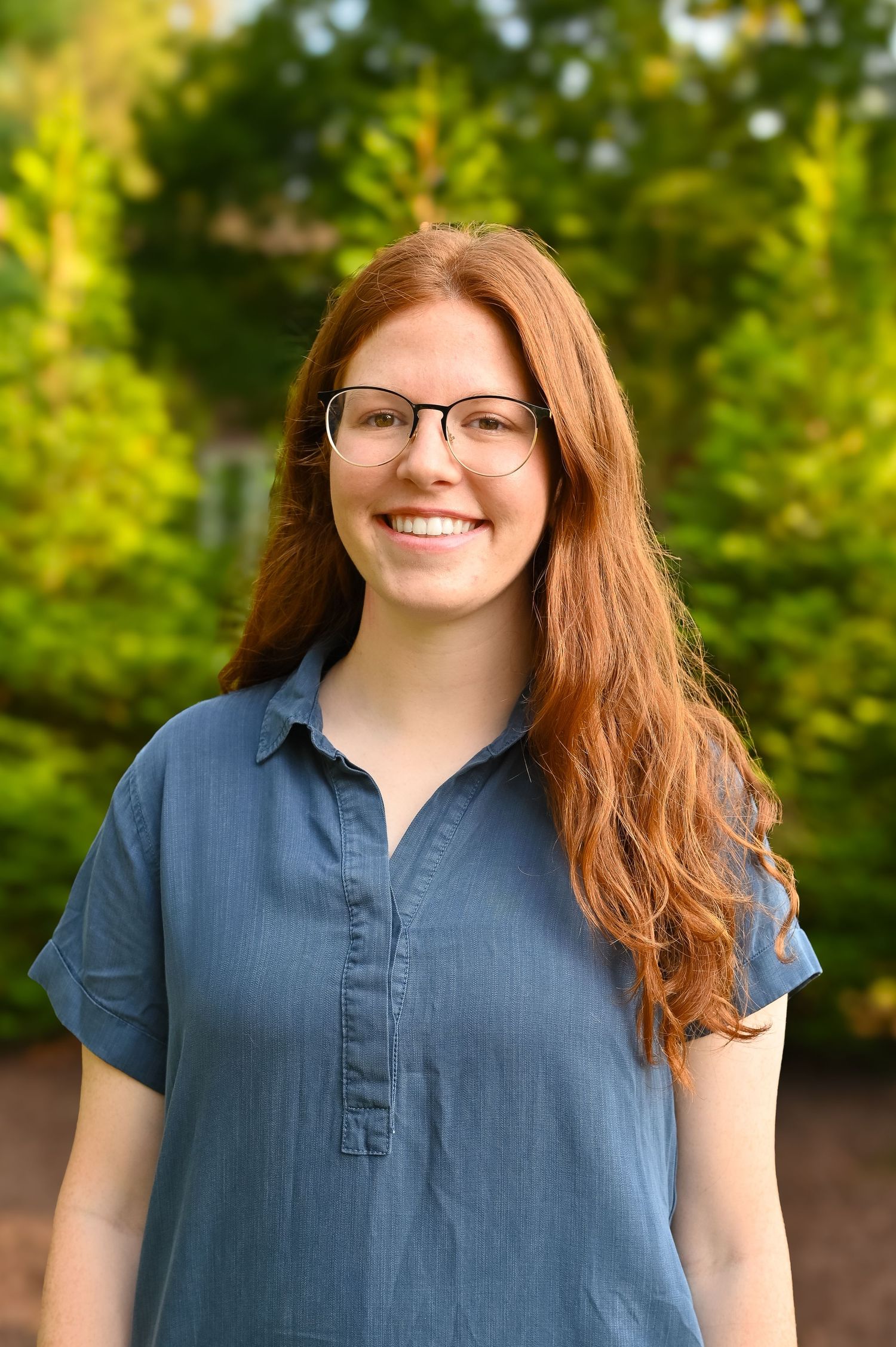 Outdoor portraits in a lush green garden setting wearing a casual blue shirt.