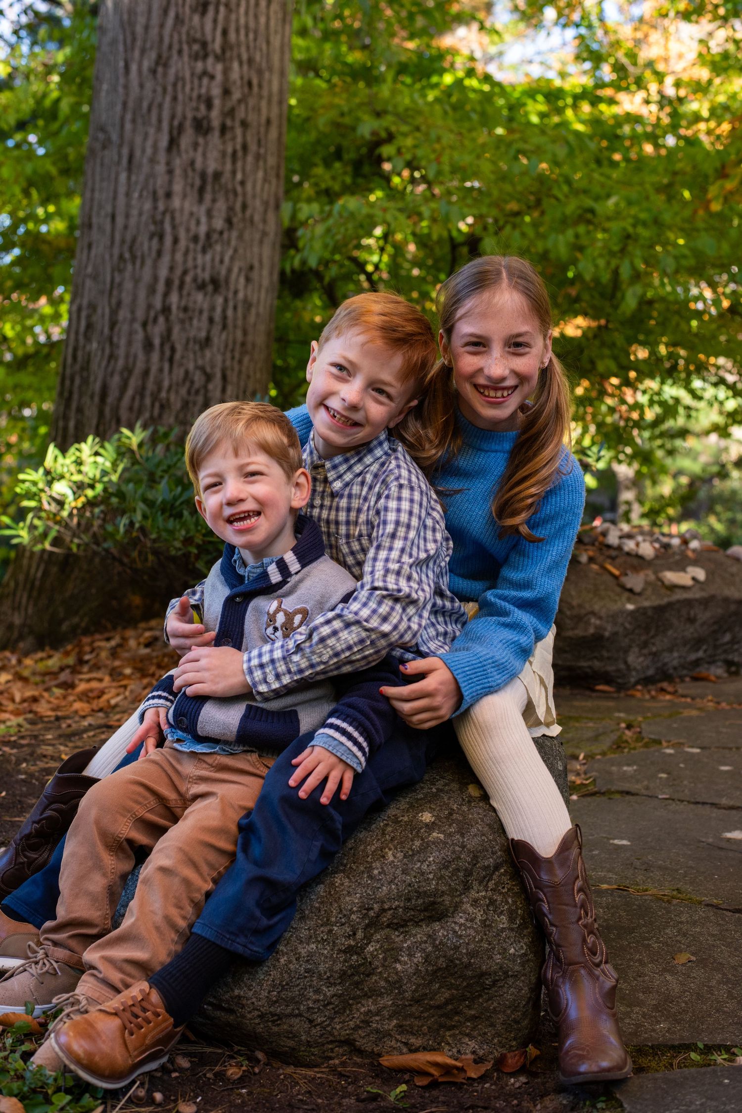 Children playing and laughing together on a large rock surrounded by fall foliage.