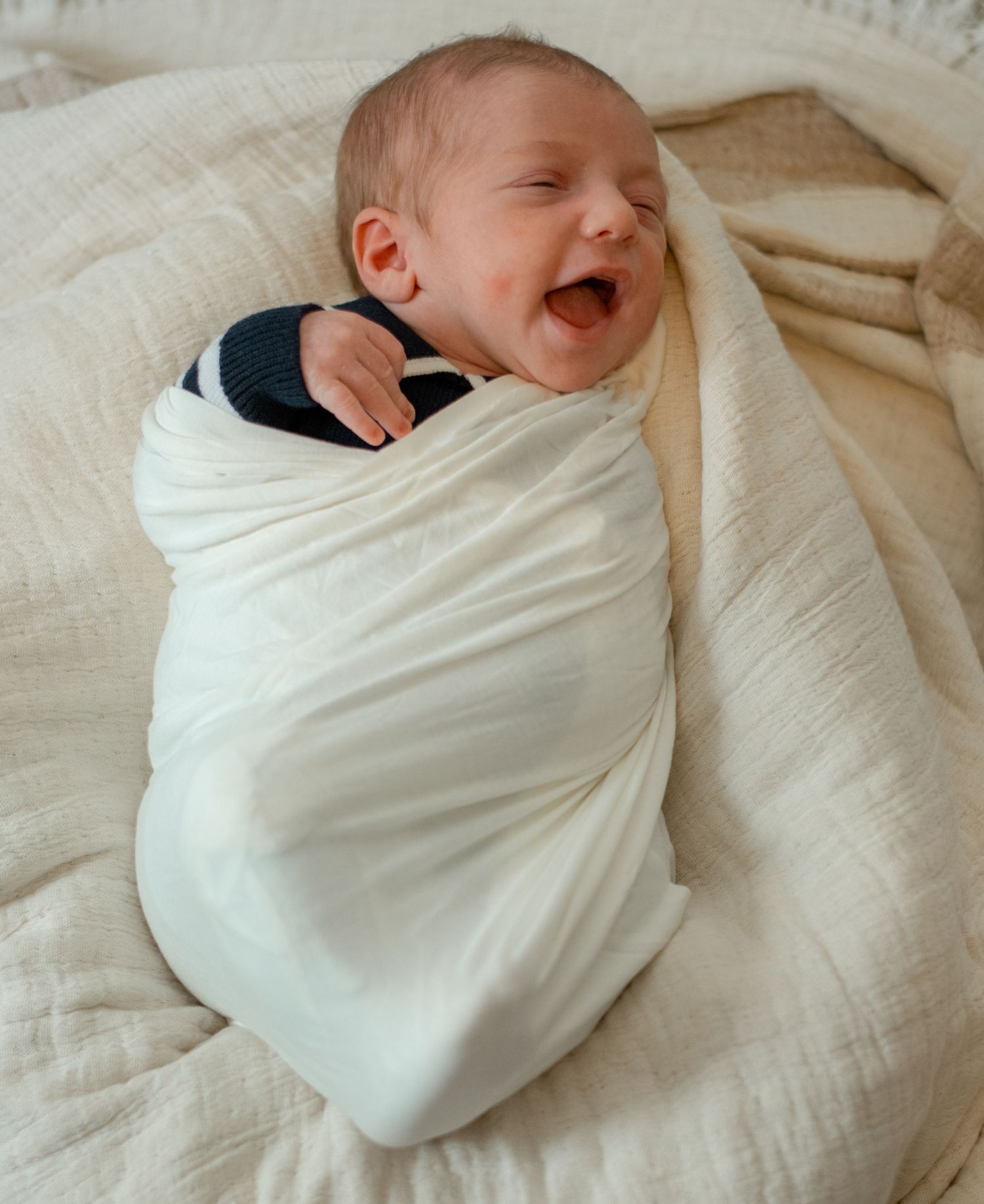 Newborn baby wrapped in white swaddle blanket sleeping peacefully.