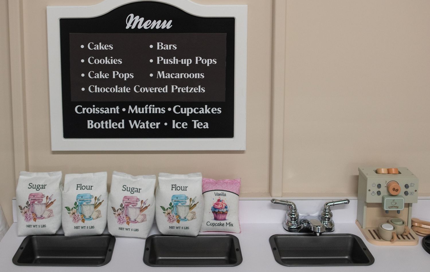 Black menu board displaying various food and beverage items including cakes, cookies, and bottled water.
